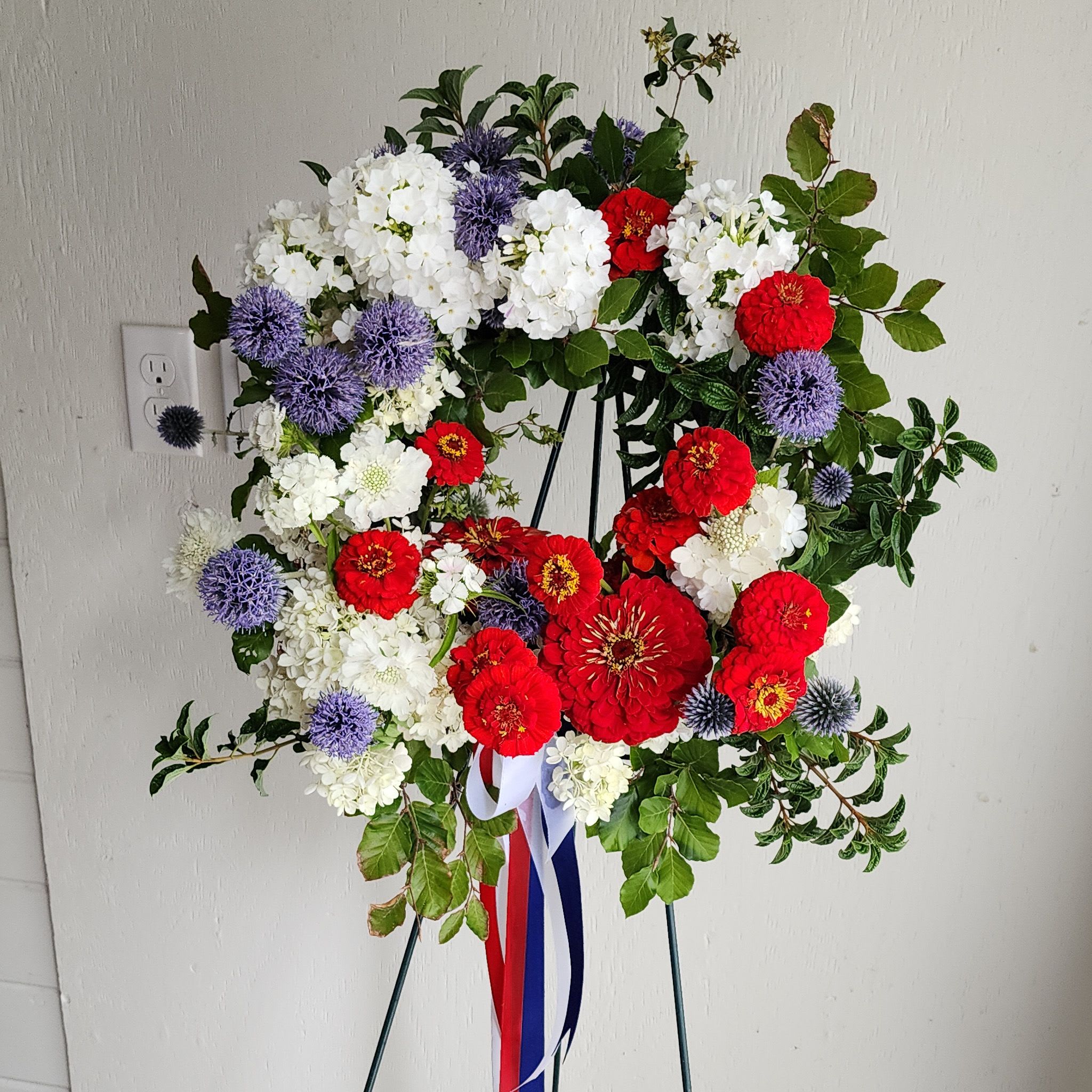 Circular floral wreath on an easel with red, white, and purple flowers