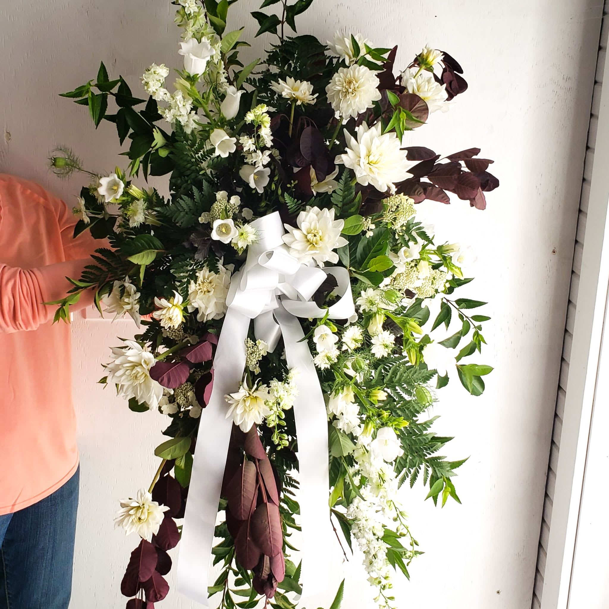 White floral wreath with a large white ribbon bow