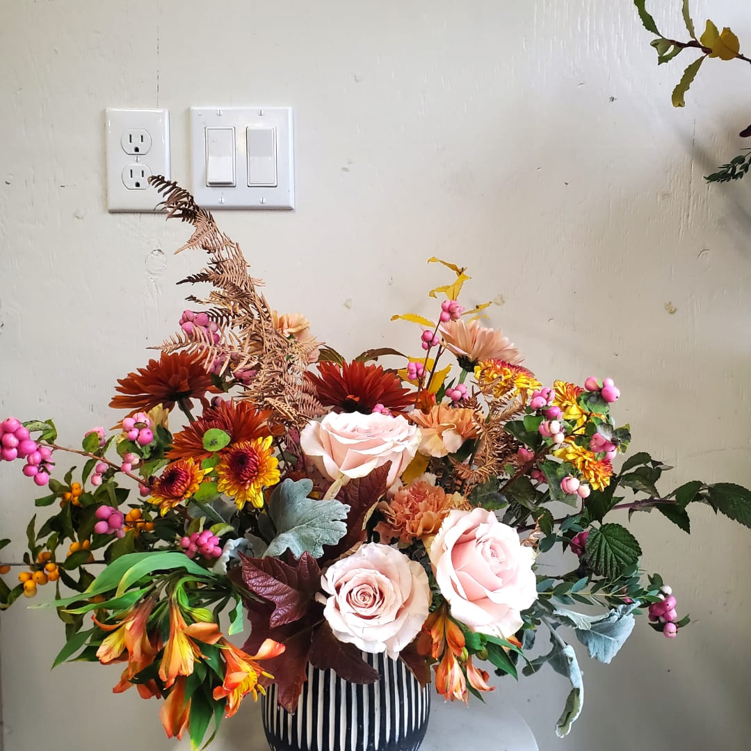 Mixed bouquet with pale pink roses and autumn-colored flowers in a striped vase