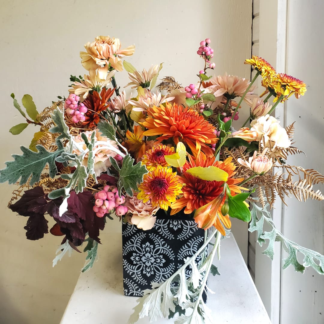 Mixed orange and peach flowers in a patterned black vase