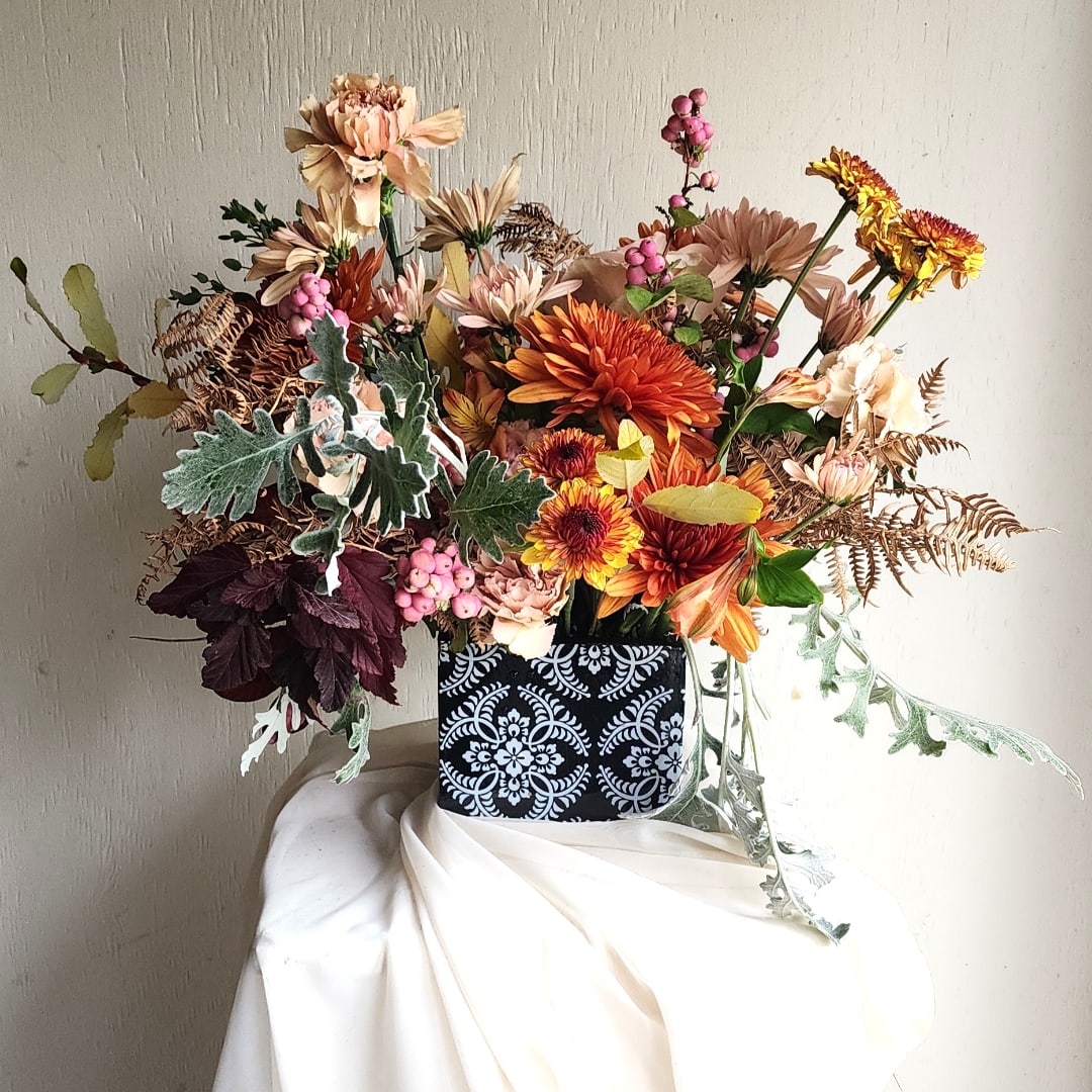 Mixed bouquet of orange and peach flowers in a patterned black container