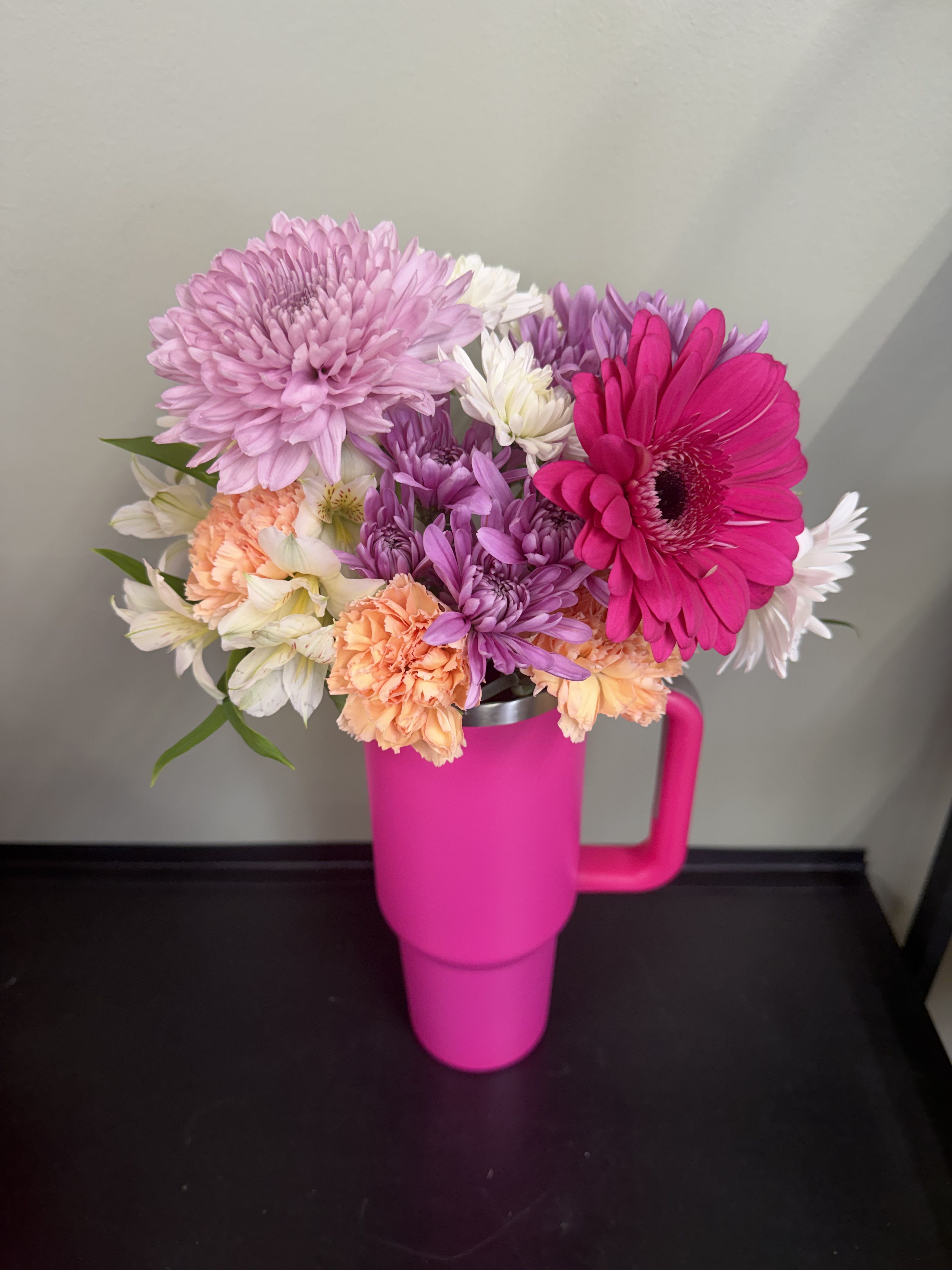 Bouquet of pink, purple, white, and peach flowers in a bright pink tumbler