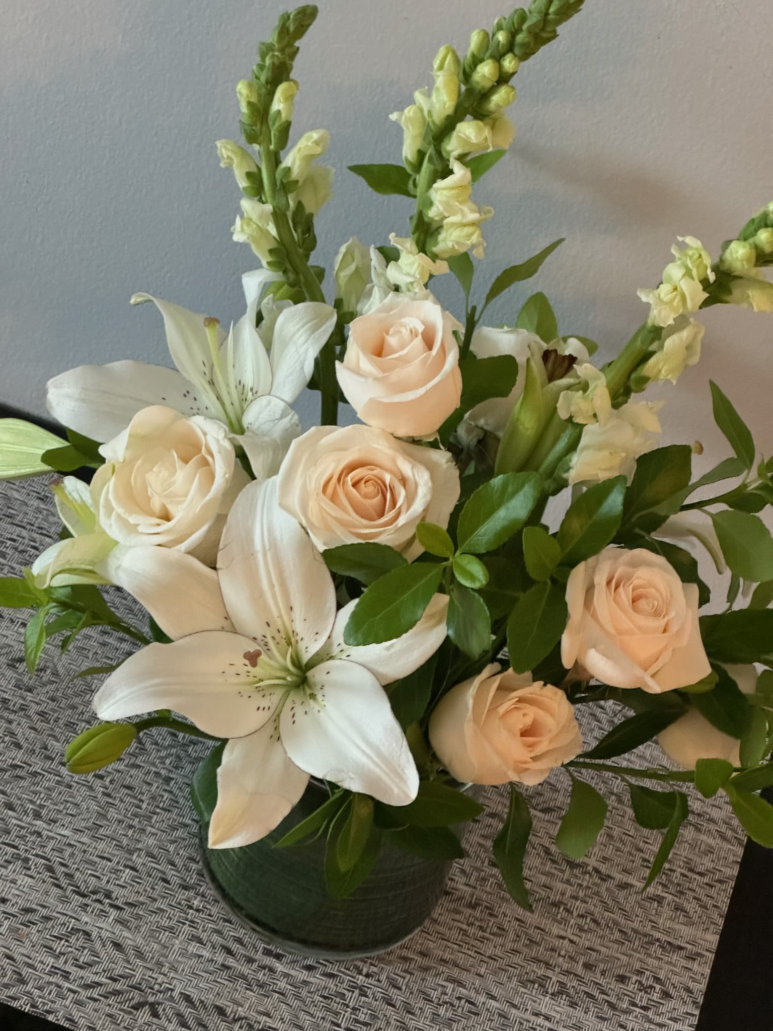Cream roses and white lilies arranged in a dark vase