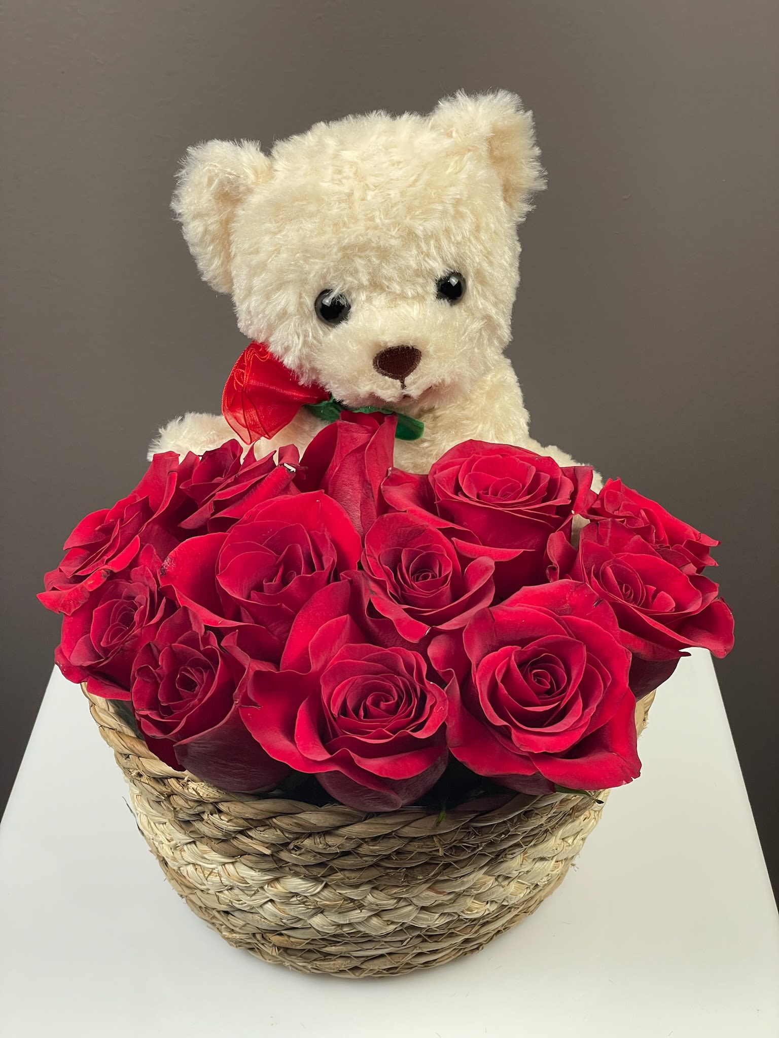 White teddy bear in a basket of red roses