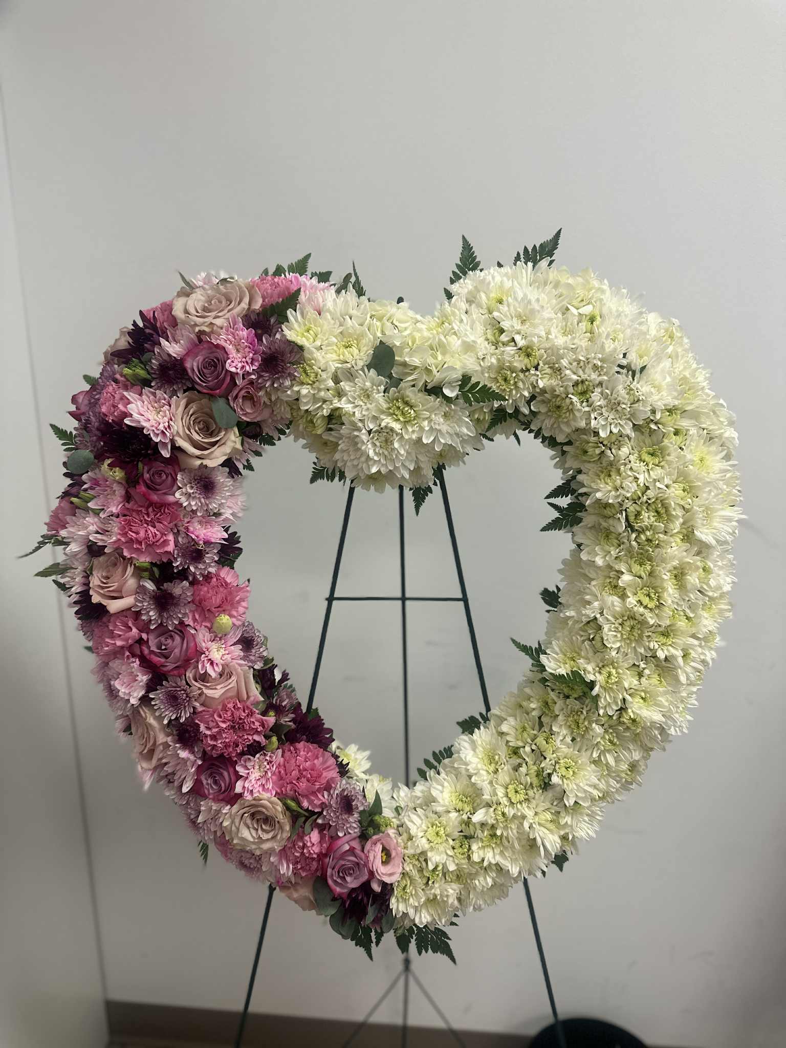Heart-shaped floral wreath with pink and white flowers on a stand