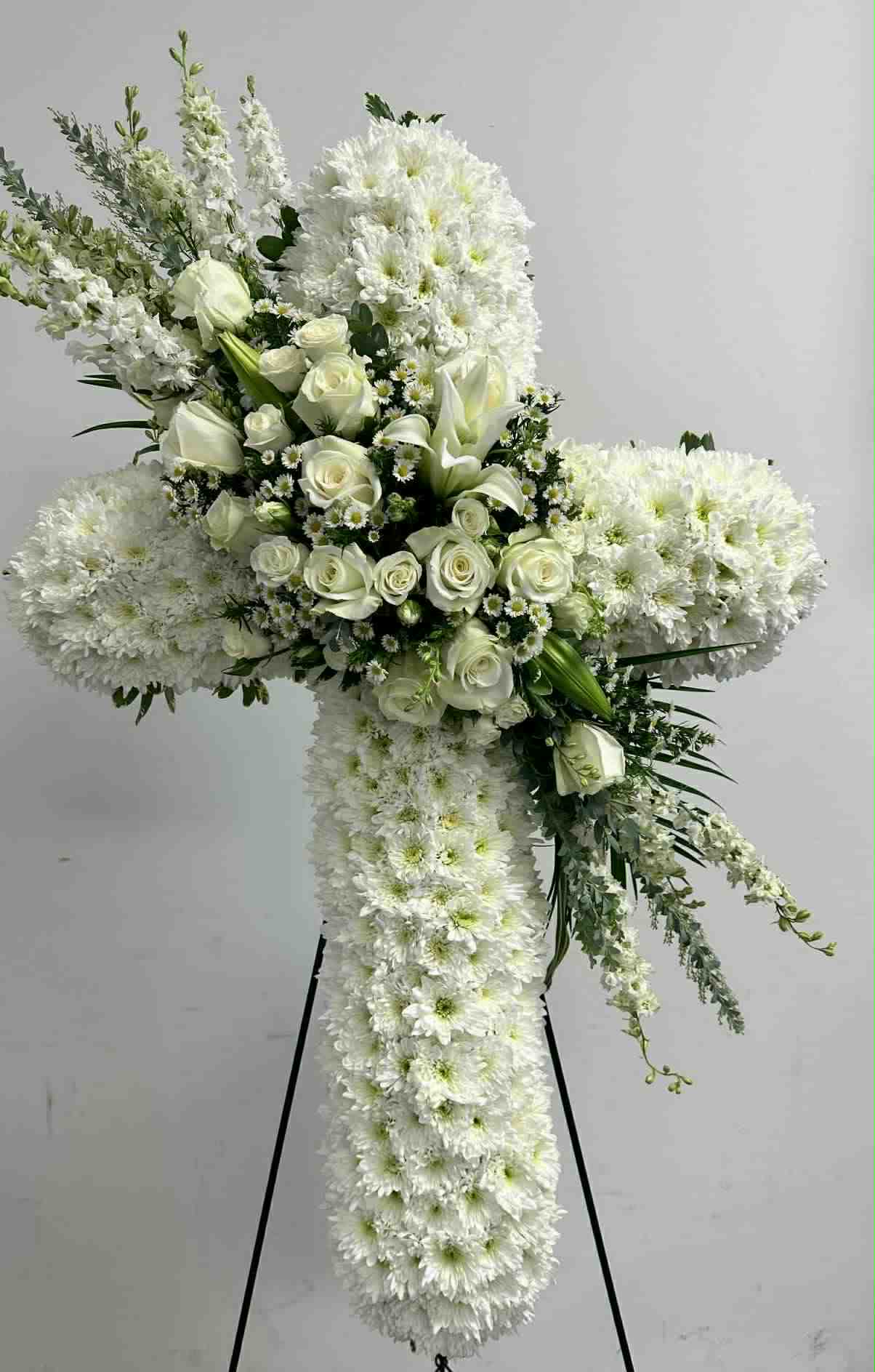 White floral cross on a stand with roses and chrysanthemums