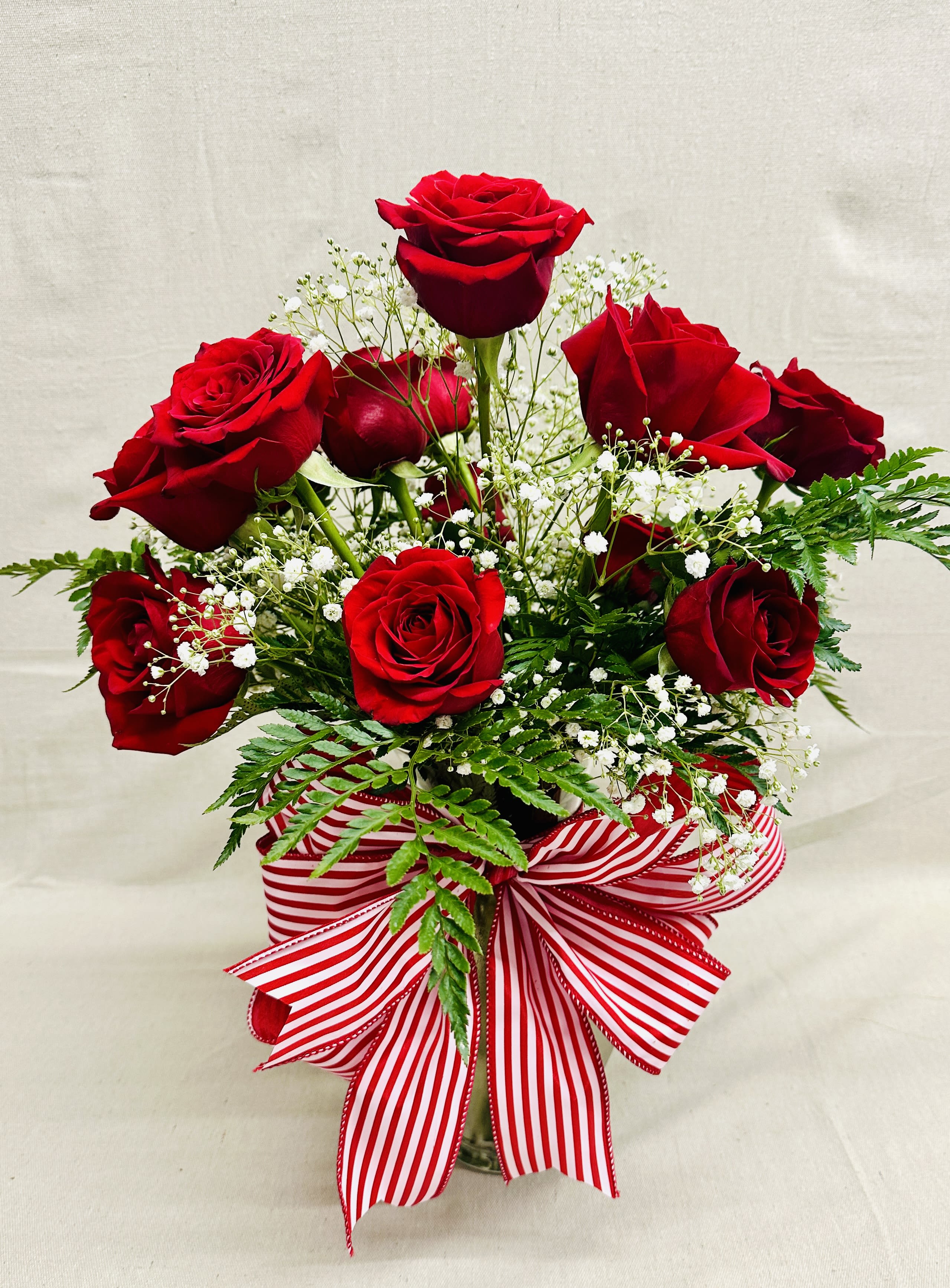 Red roses arranged in a vase with baby's breath and a striped ribbon