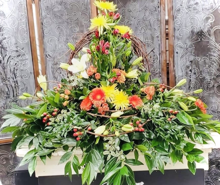 Large floral spray with lilies and bright daisy blooms in a wicker frame