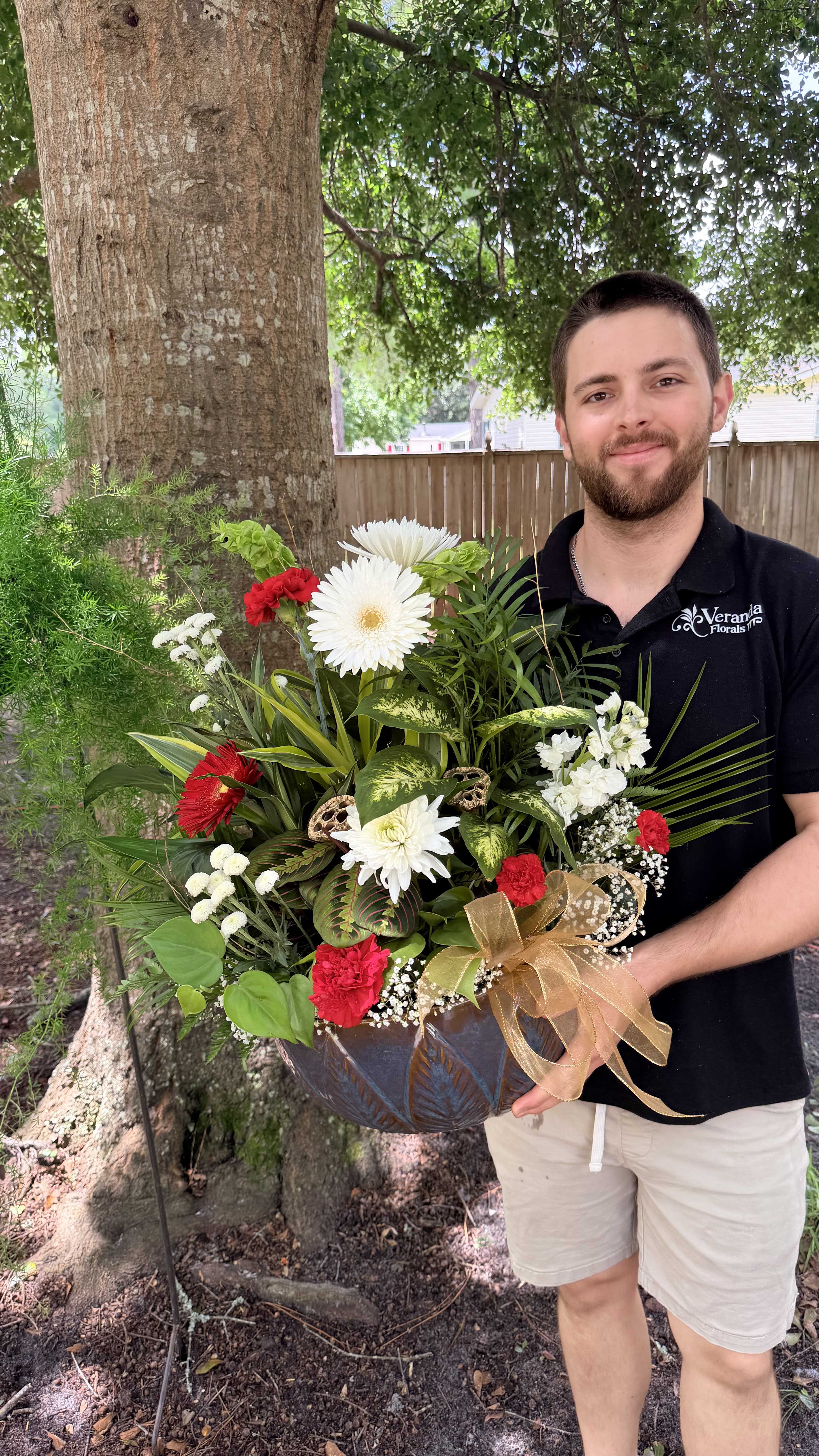 Large mixed flower arrangement in a dark bowl vase with a gold ribbon