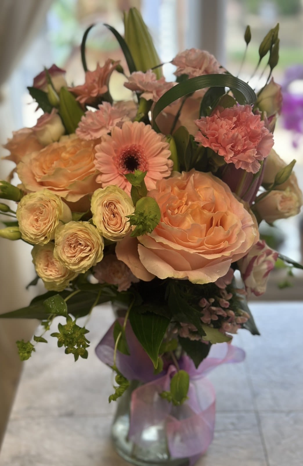 BLUSHING BEAUTY BOUQUET - A BEAUTIFUL BOUQUET OF BLUSH PINKS AND PEACH HUES IN A BOW WRAPPED GATHERING VASE. ROSES, SPRAY ROSES, GERBERAS, LISIANTHUS, CARNATIONS, MINI CARNS AND GREENS. BRINGING SPRING VIBES EARLY!