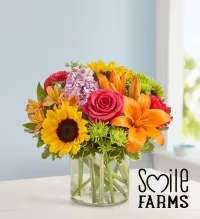 Mixed bouquet in a clear glass vase with sunflowers, roses, and lilies