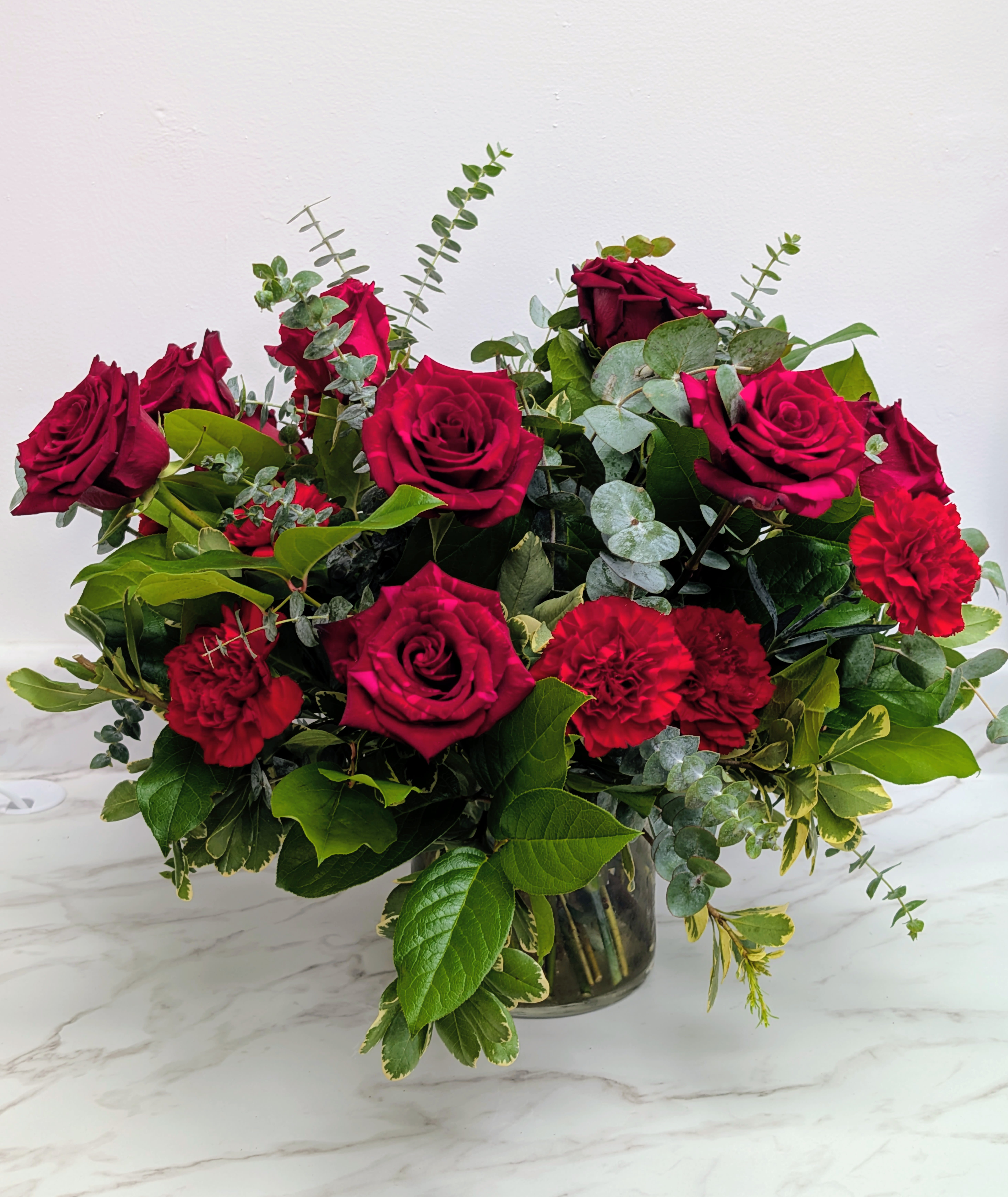 Red roses and carnations in a glass vase with mixed greenery