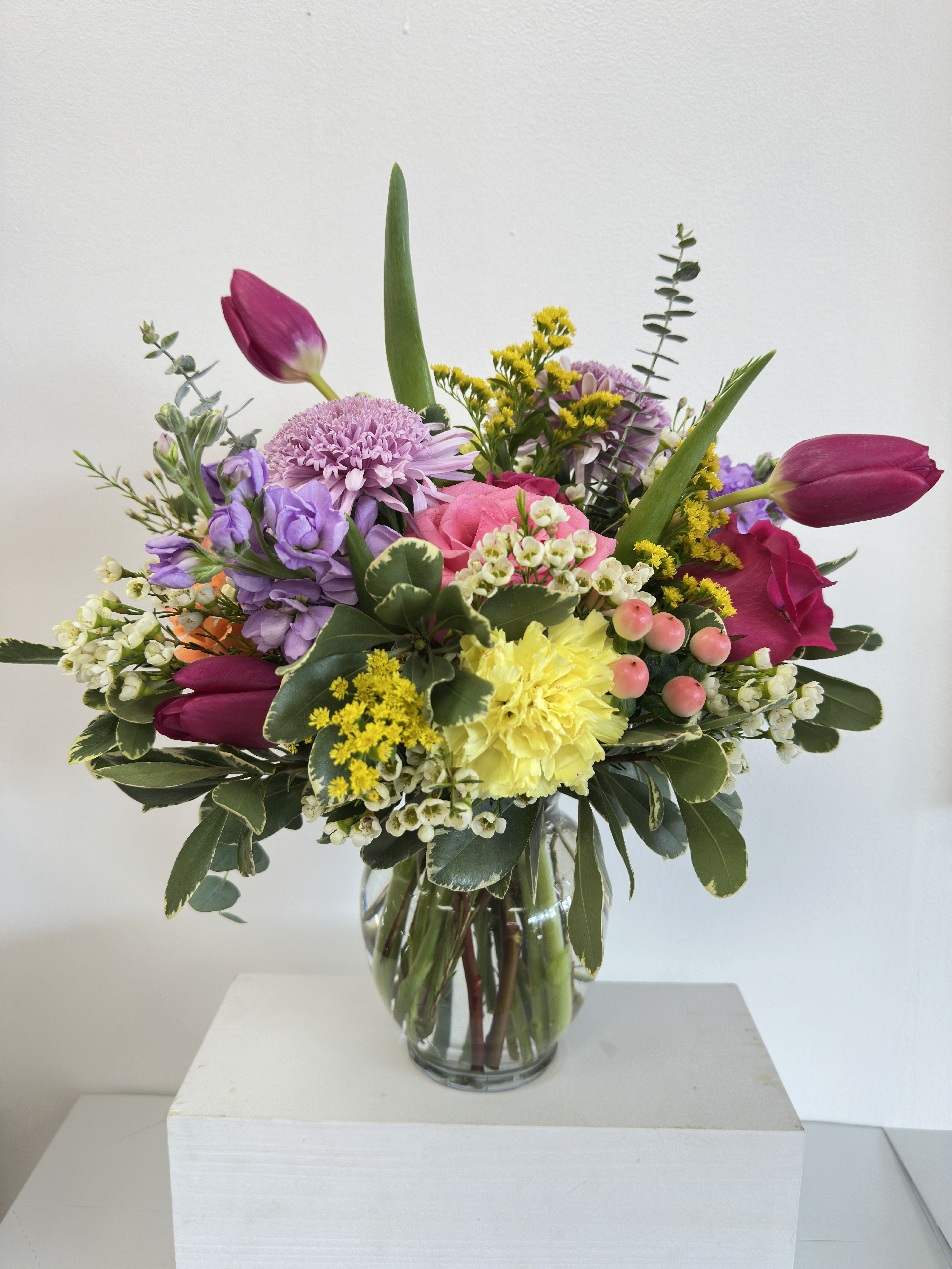Colorful mixed bouquet with pink roses, yellow carnation, tulips and lavender blooms in a clear glass vase
