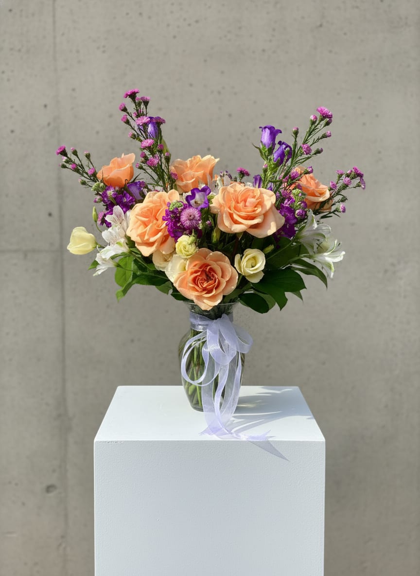 Peach and purple bouquet in a clear glass vase with a ribbon