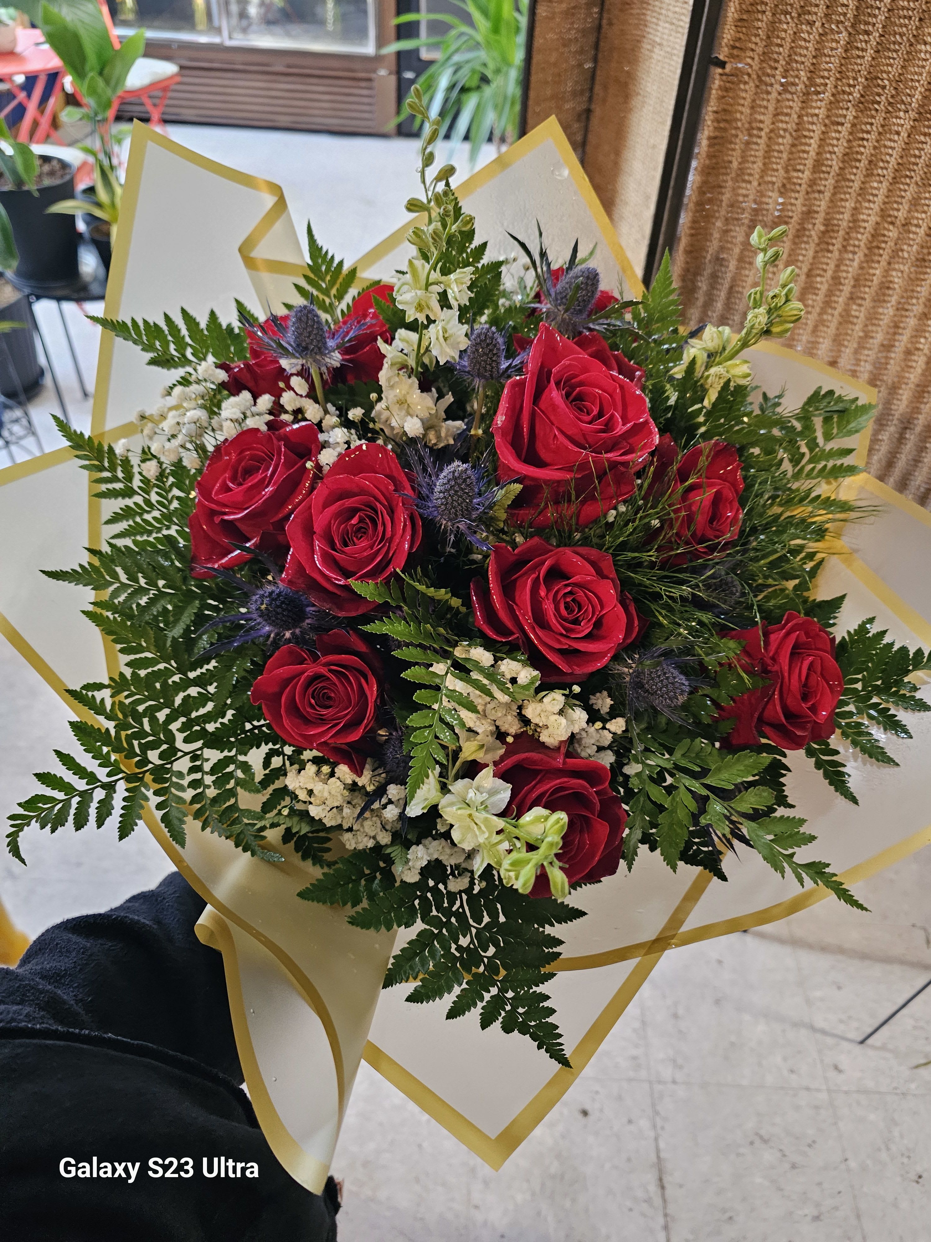Bouquet of red roses with white filler flowers and greenery in gold-trimmed wrap