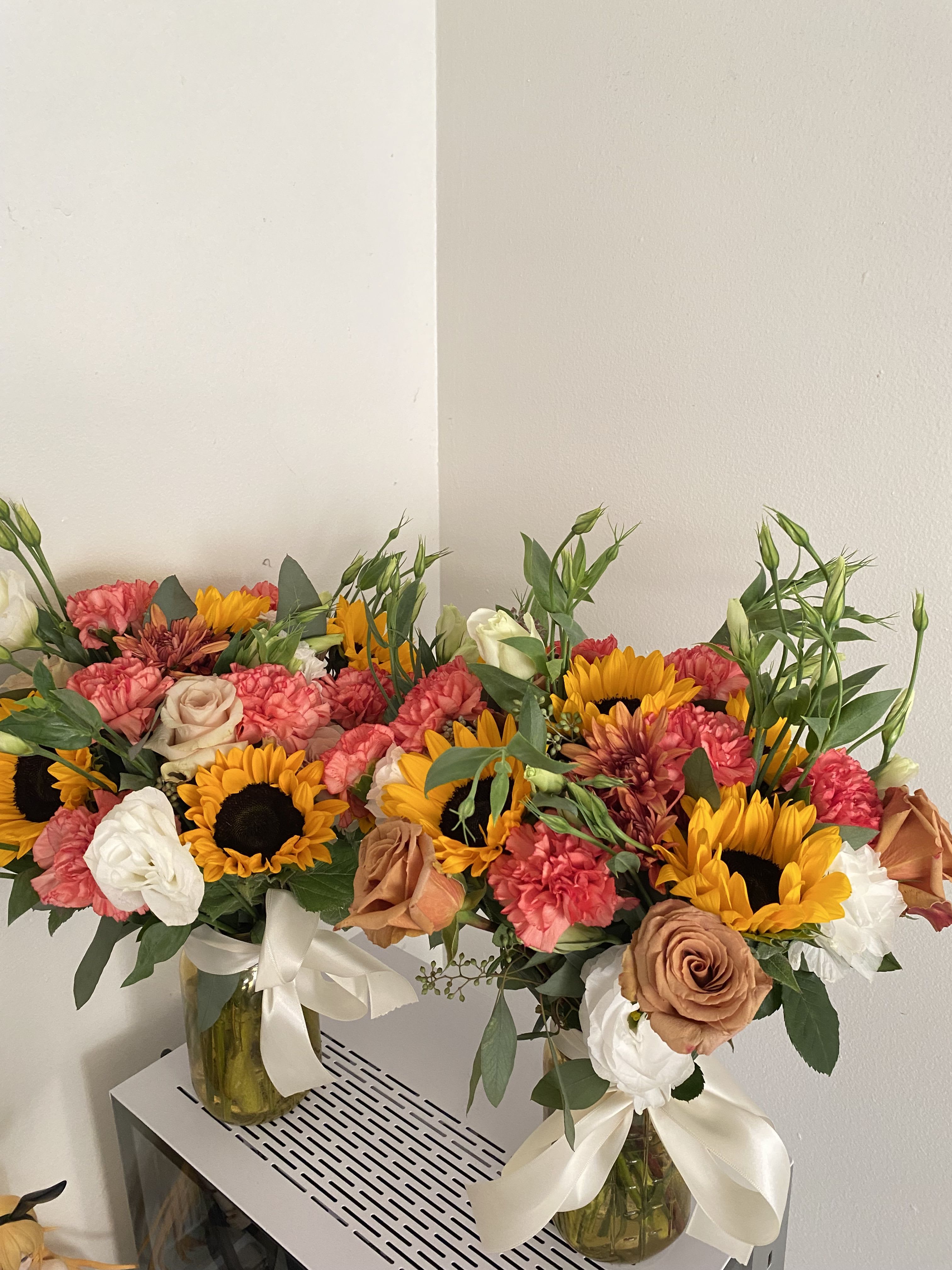 Two mixed flower arrangements in glass vases with sunflowers, roses, and carnations
