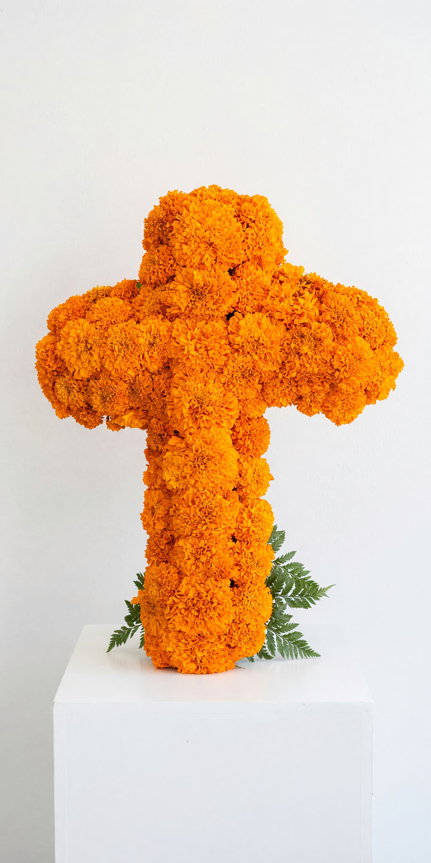 Orange marigold cross arrangement on a white pedestal