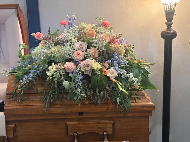 Large pastel floral arrangement on a wooden casket