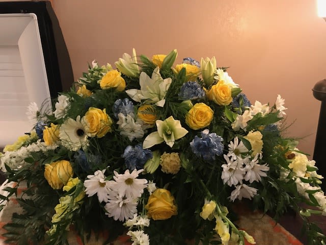 Large mixed floral arrangement with yellow roses, white lilies, and blue flowers