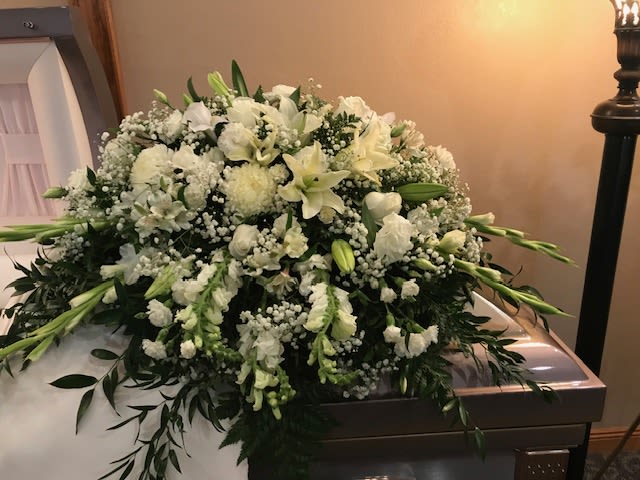 Large white funeral casket spray with lilies and baby’s breath