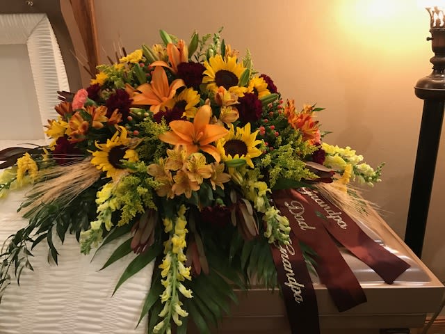 Large floral casket spray with sunflowers, lilies, and orange blooms