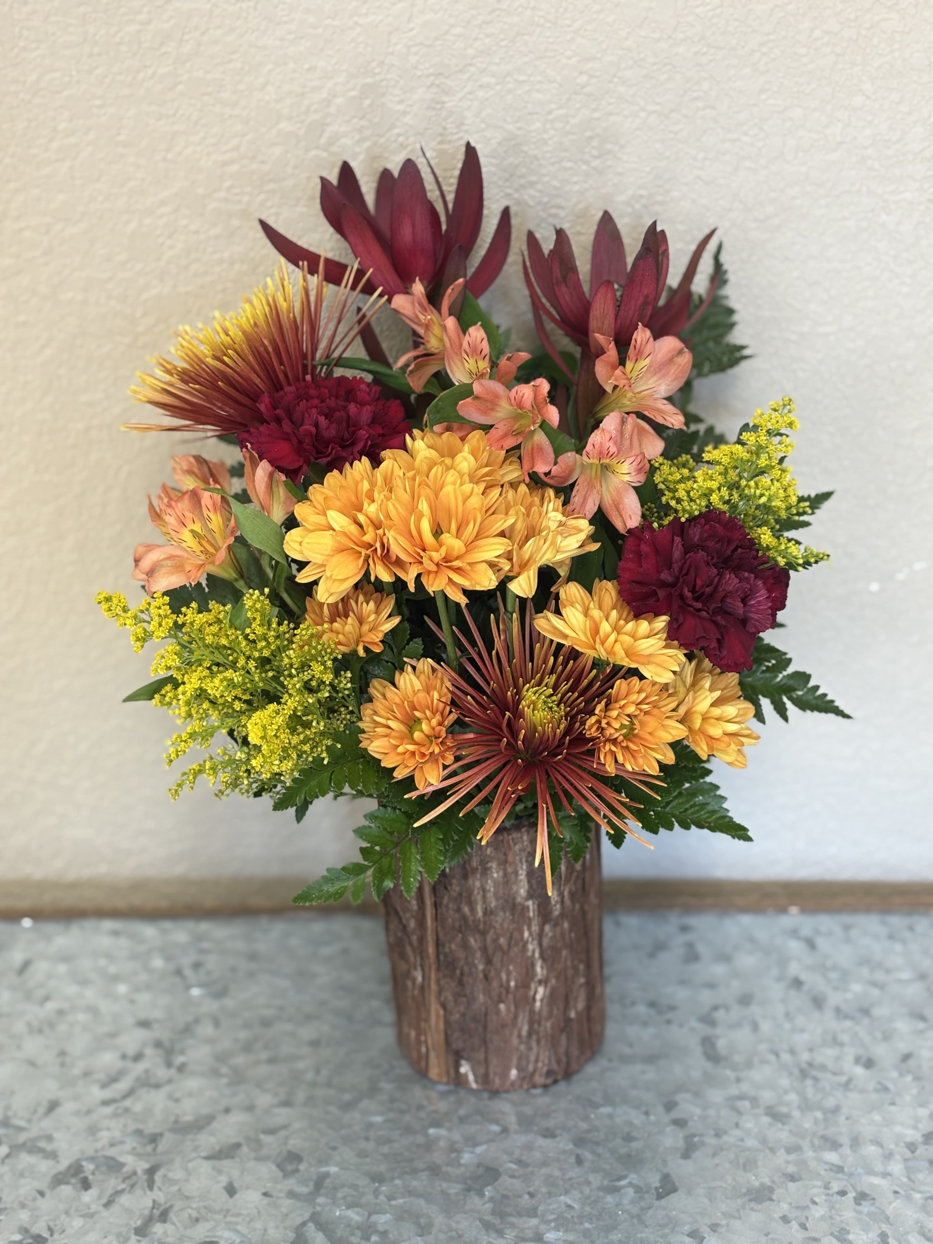 Mixed bouquet of orange, burgundy, and yellow flowers in a rustic wooden vase