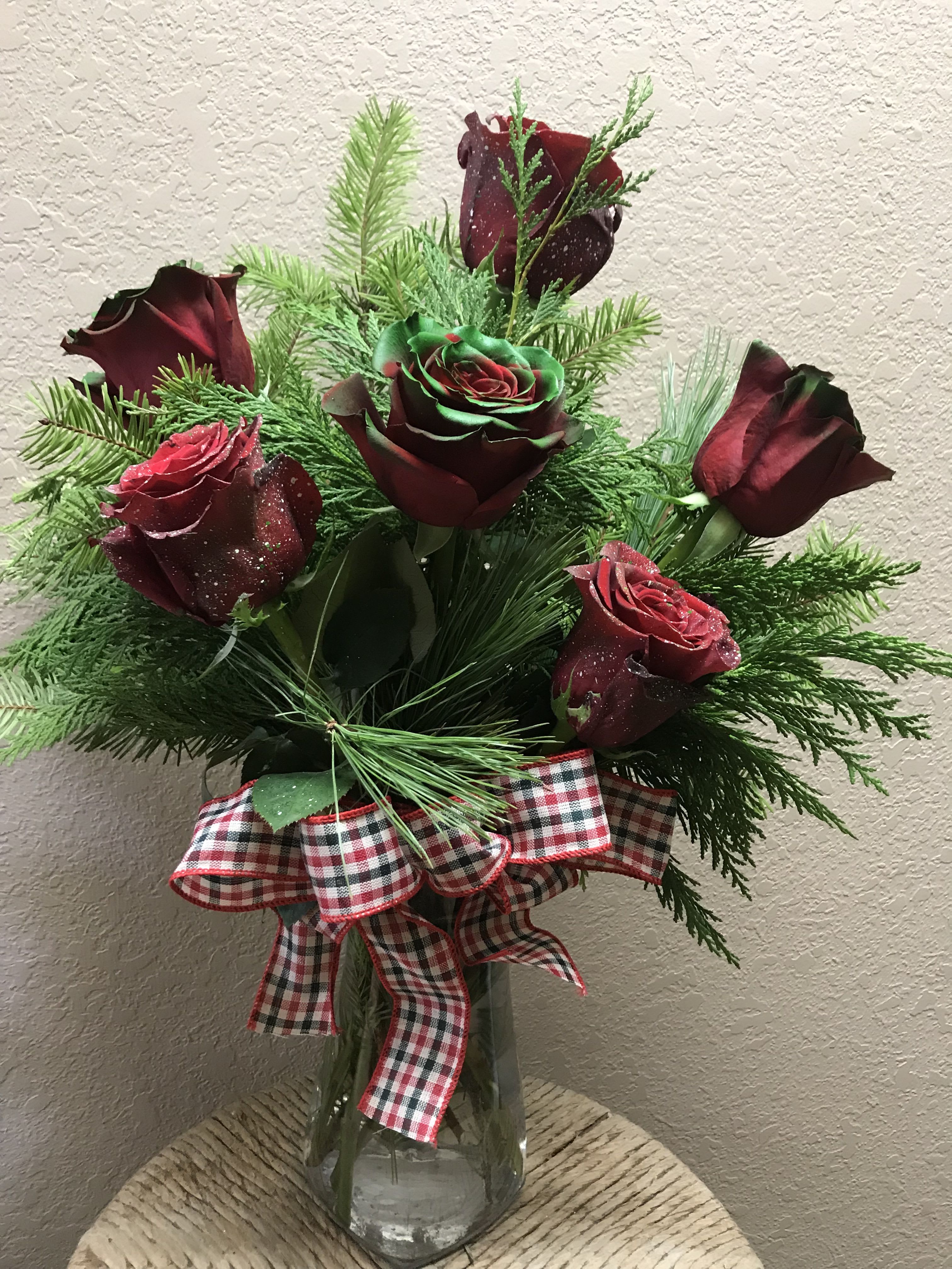 Bouquet of dark red roses with evergreen and a plaid ribbon in a glass vase