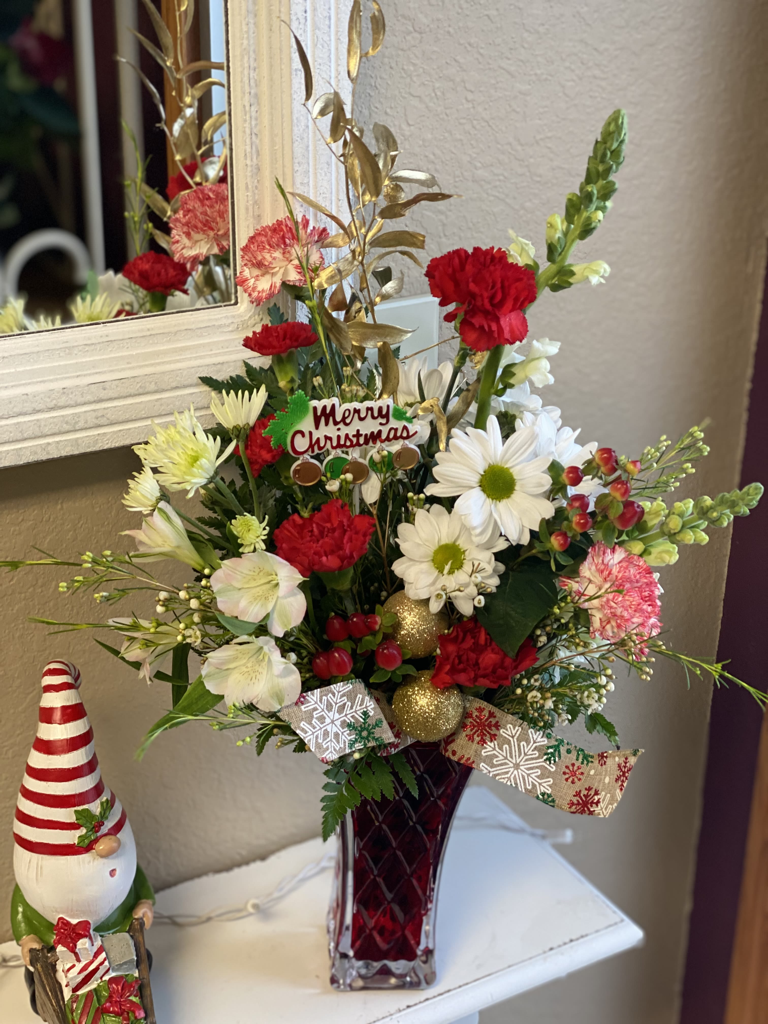 Christmas floral arrangement in a red vase with a Merry Christmas pick
