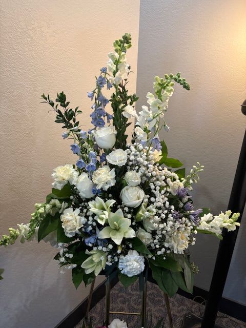 Tall white and blue floral funeral spray on a stand
