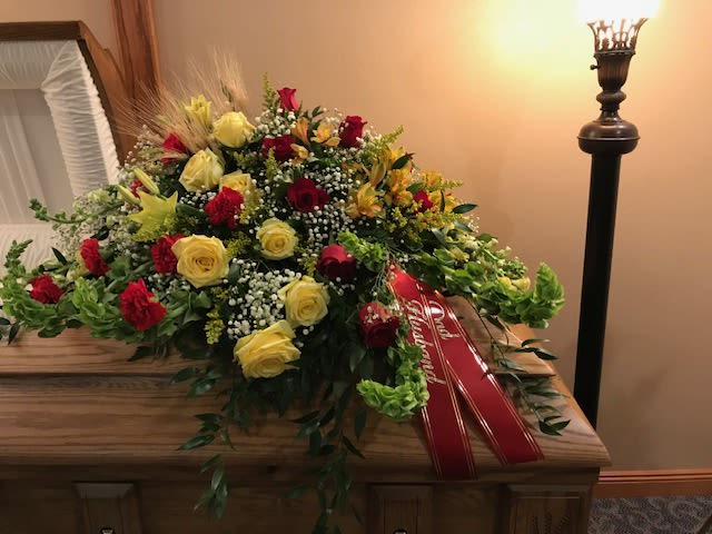 Large red and yellow floral casket spray with ribbon on a wooden casket
