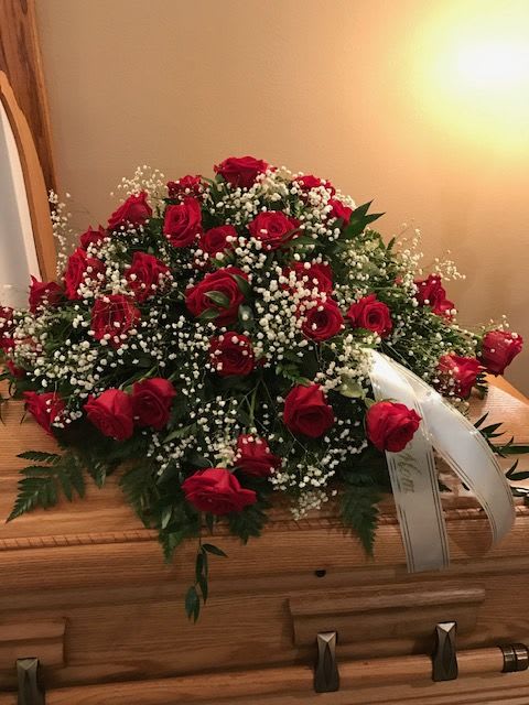 Red rose casket spray with white baby's breath on a wooden casket