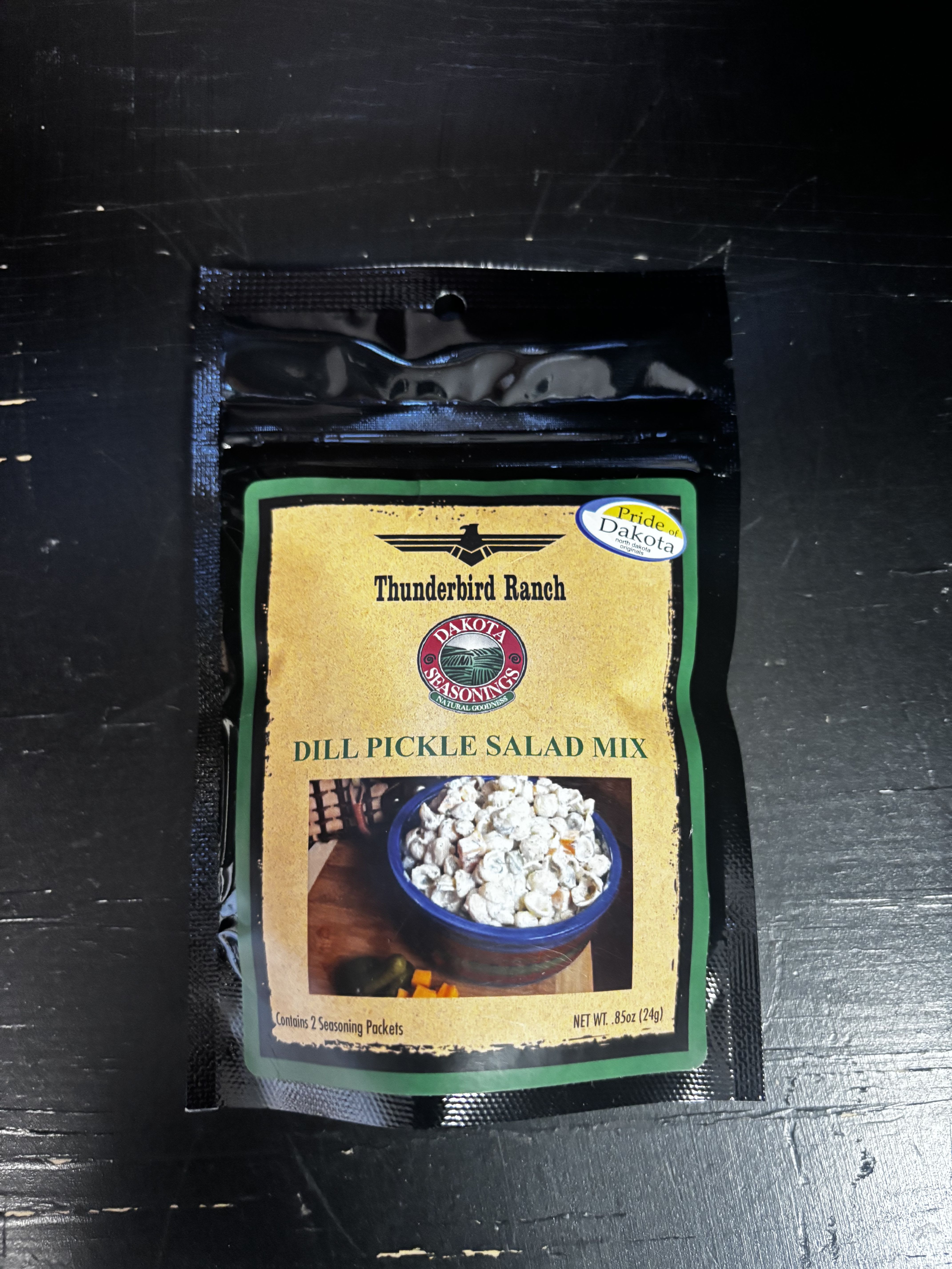 A packet of dill pickle salad mix on a dark surface.