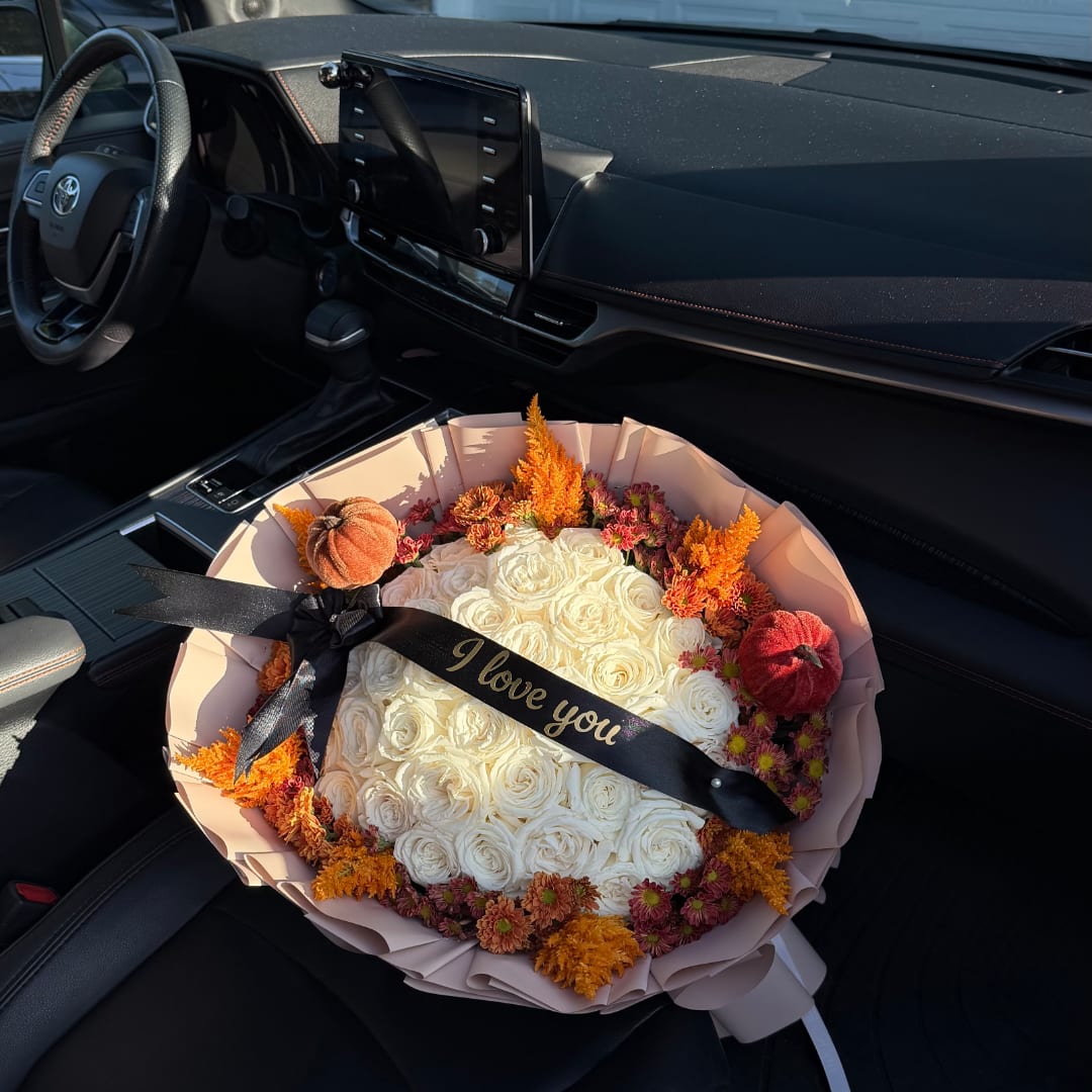 Bouquet of white roses with orange accents and a black ribbon in a car seat