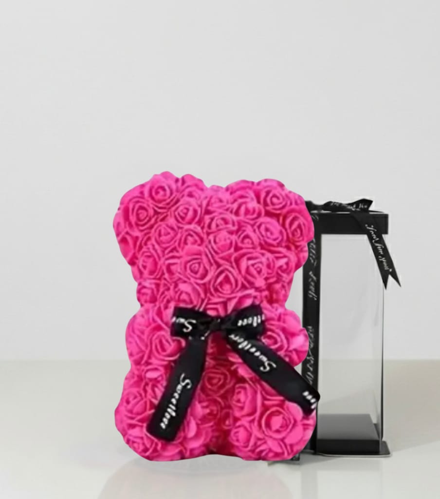 Pink rose teddy bear with a black ribbon beside a clear gift box