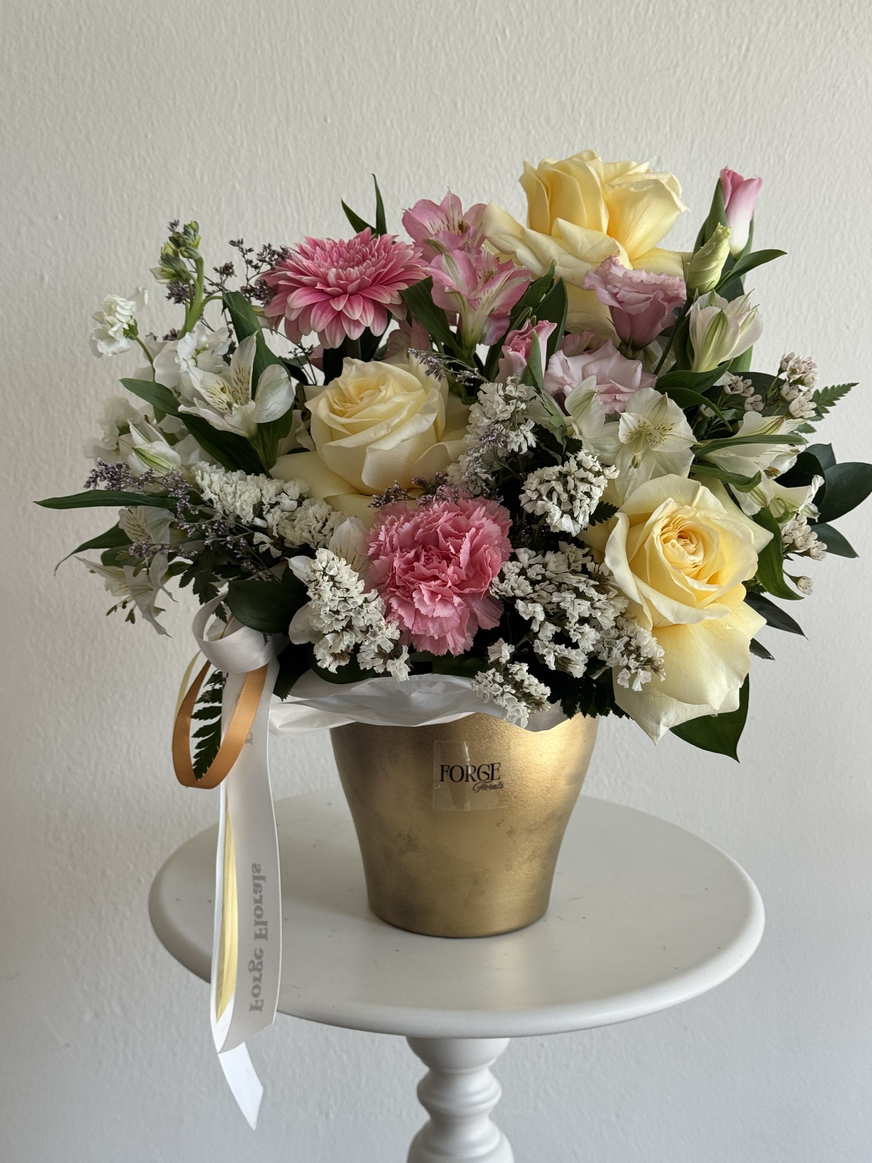 Pink and cream flower arrangement in a gold vase with ribbon