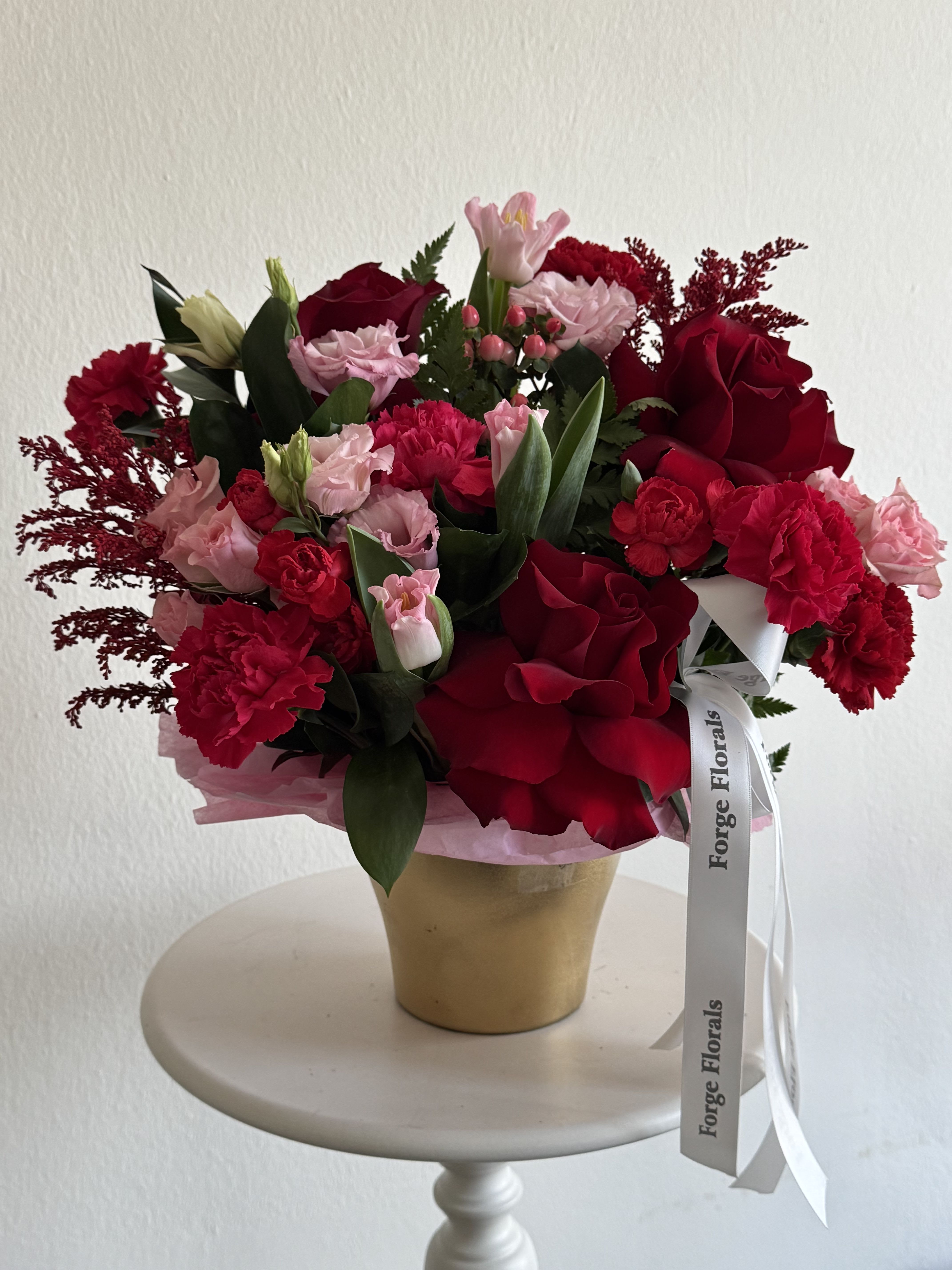 Red and pink mixed flower arrangement in a gold vase with a ribbon