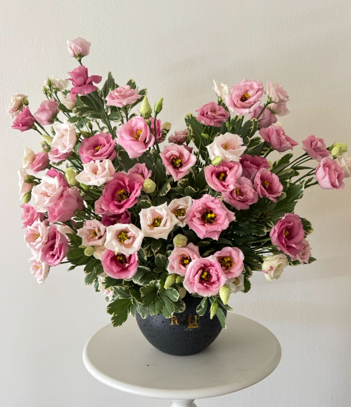 MonoLisa- Lisiantus and pittosporum in a pot - An airy and elegant arrangement featuring delicate pink lisianthus accented with fresh seasonal greenery. Designed in a modern keepsake vase, this graceful floral piece brings softness and charm to any celebration, making it a beautiful gift for birthdays, anniversaries, thank-you gestures, or simply to brighten someone’s day.  Please note: Flower varieties may vary slightly based on seasonal availability while maintaining the overall style, color palette, and value of the arrangement.