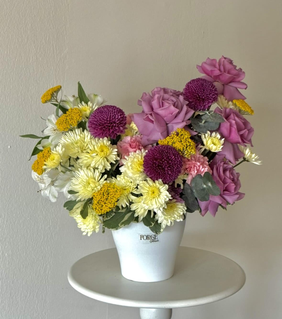 Sunny daydeams- chrysanthemum, roses, mini chrysanthemum  - A cheerful garden-inspired arrangement featuring soft lavender roses, vibrant seasonal blooms, playful button mums, and fresh greenery in a modern ceramic container. Designed to brighten any room, this charming arrangement is perfect for birthdays, thank-you gifts, celebrations, or simply bringing a little sunshine to someone’s day.  Please note: Flower varieties may vary based on seasonal availability while maintaining the overall style, color palette, and value of the arrangement.