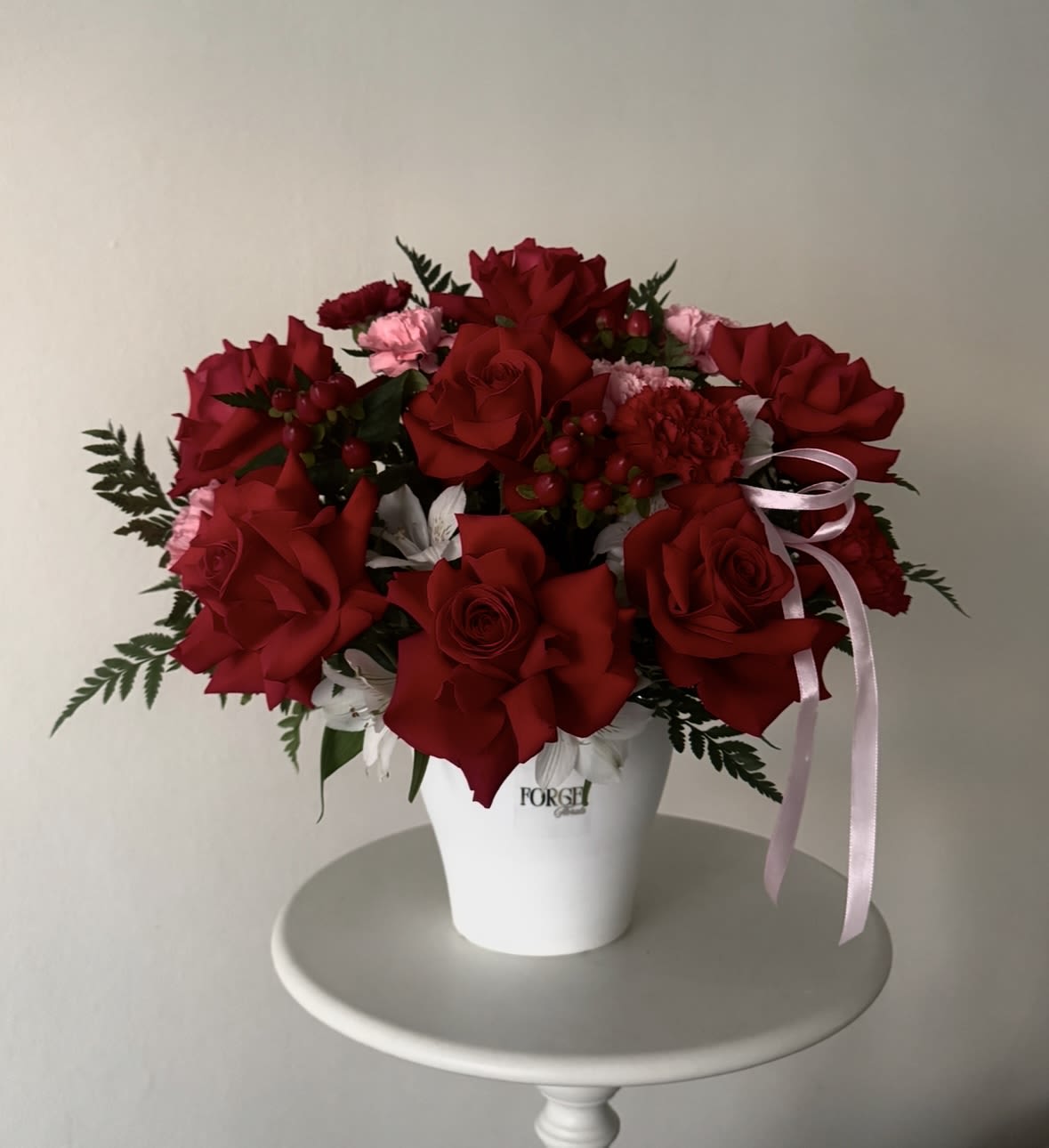 Forever Yours- red rose arrangement - A classic arrangement of rich red roses accented with delicate seasonal blooms and lush greenery, beautifully designed in a modern ceramic container. Elegant, timeless, and full of romance, this arrangement is perfect for anniversaries, birthdays, romantic occasions, or expressing heartfelt love and appreciation.  Please note: Flower varieties may vary based on seasonal availability while maintaining the overall style, color palette, and value of the arrangement.