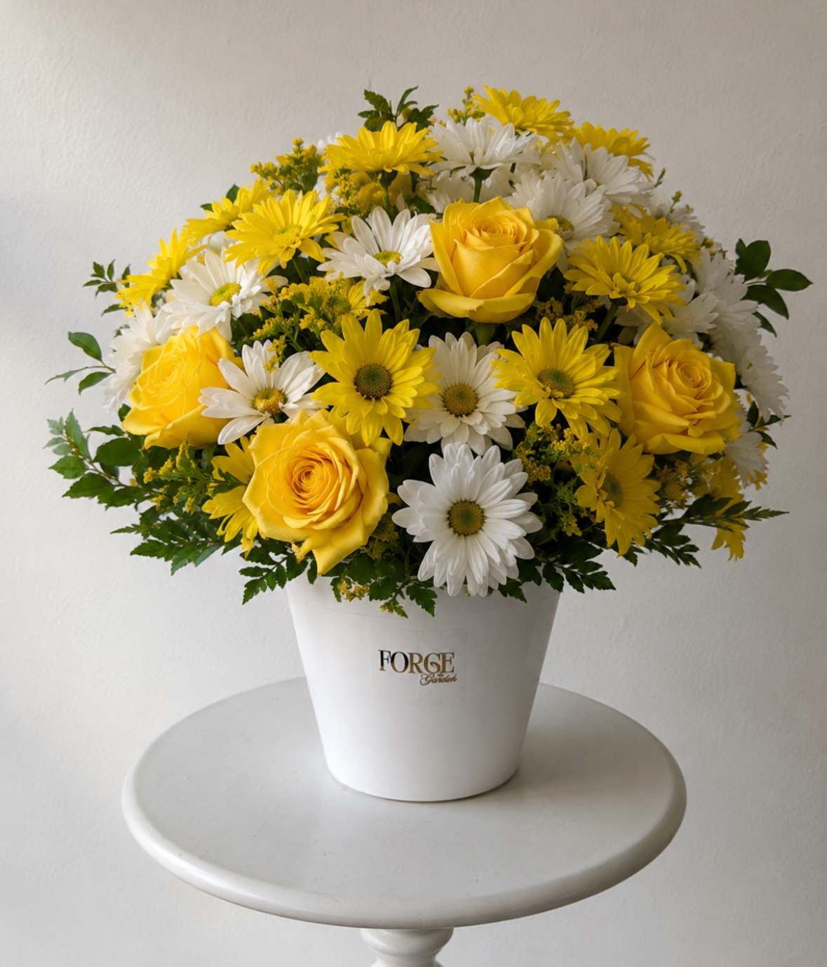 Yellow roses and white daisies arranged in a white vase