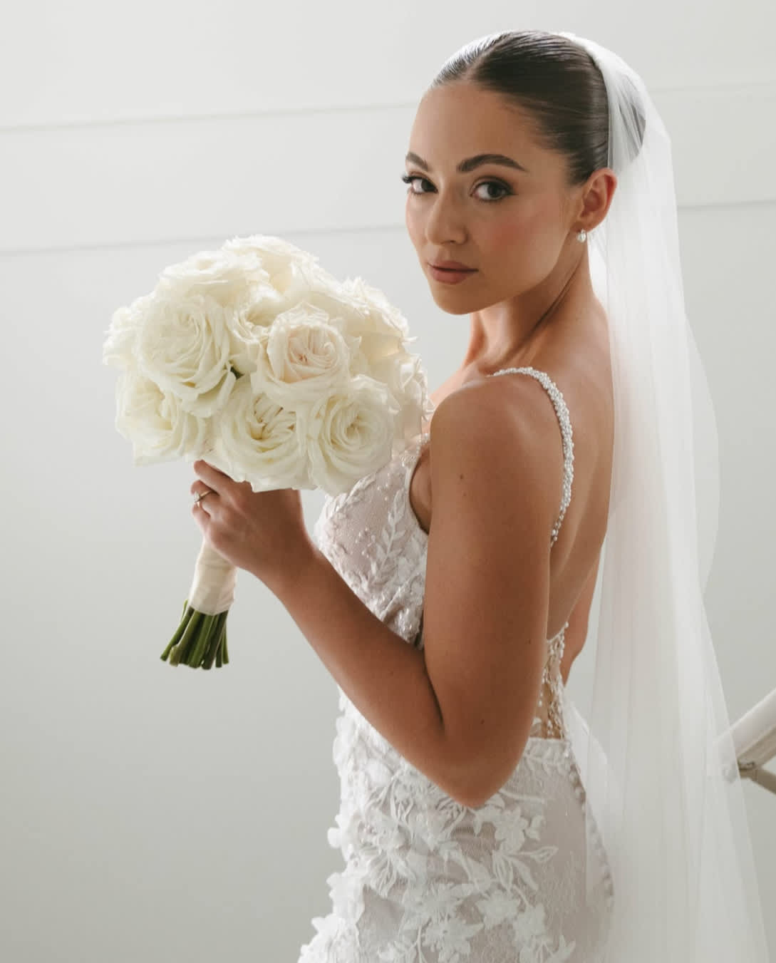 Bride holding a white rose bouquet with a veil and lace gown