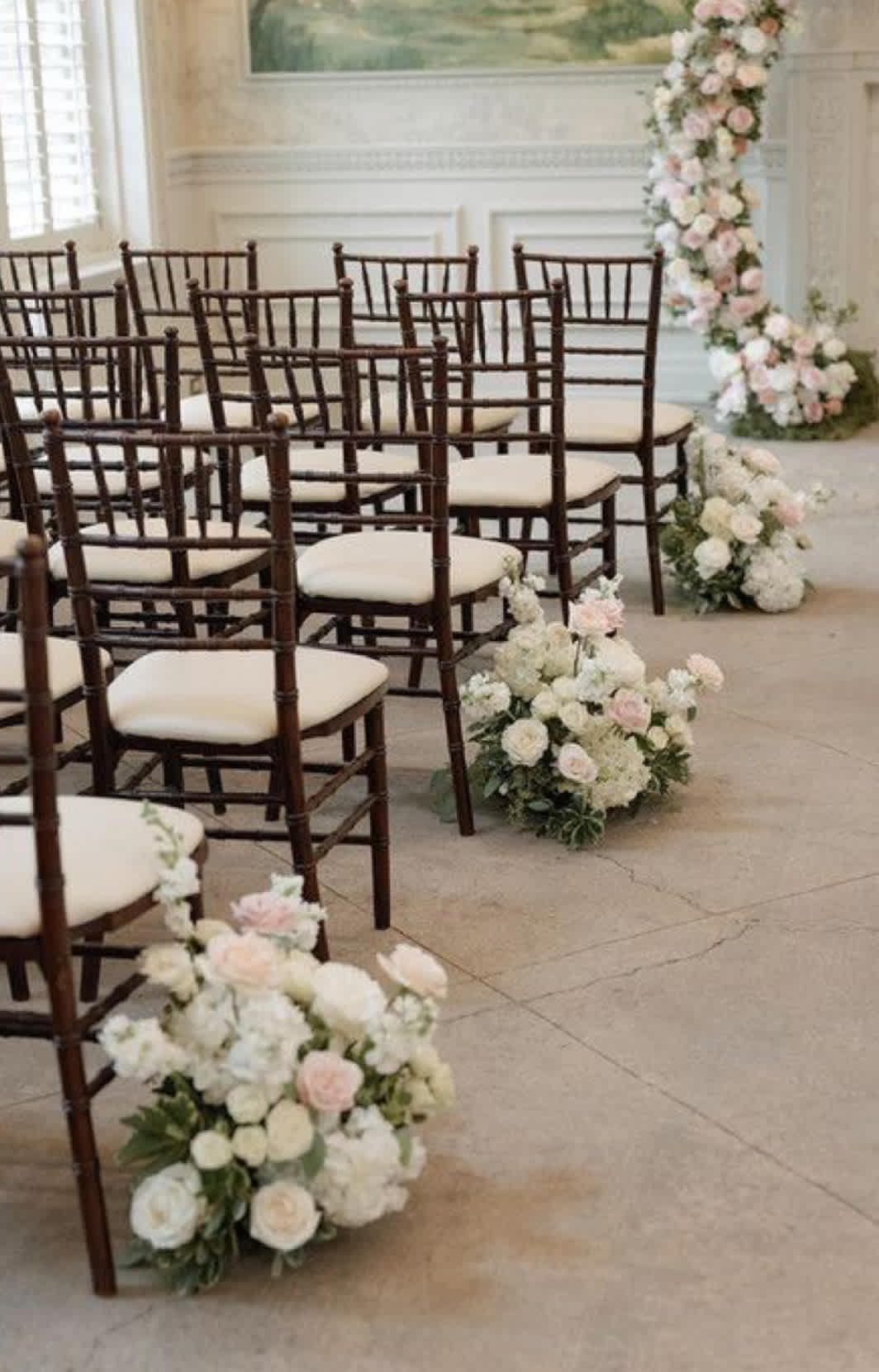 Pastel floral arrangements line rows of chairs in a ceremony space.