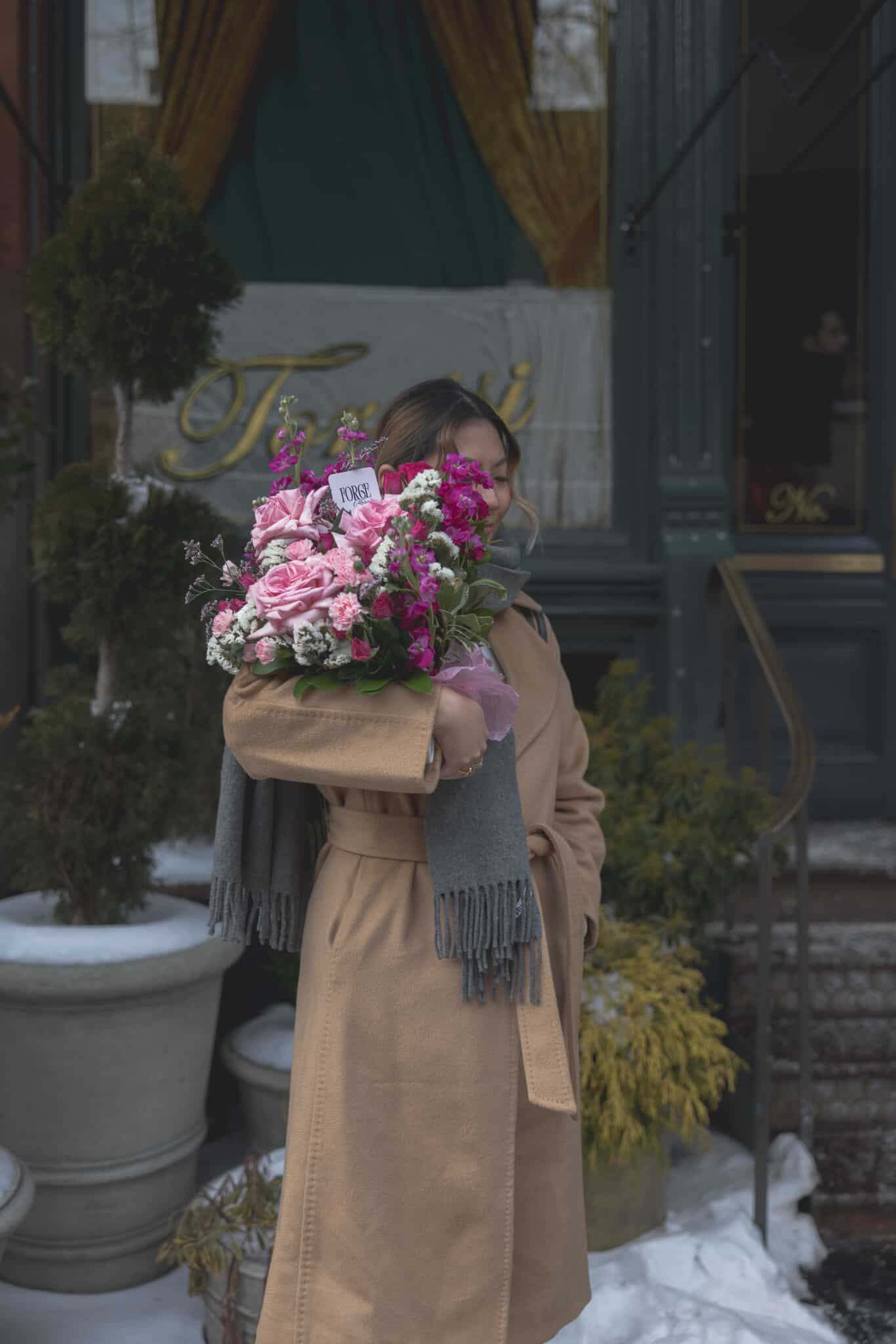 Woman holding a pink bouquet wrapped in tan paper outdoors