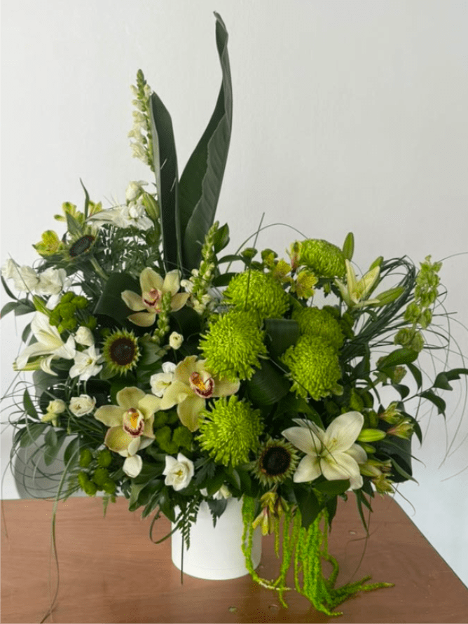 Green and white floral arrangement in a white vase with orchids and lilies