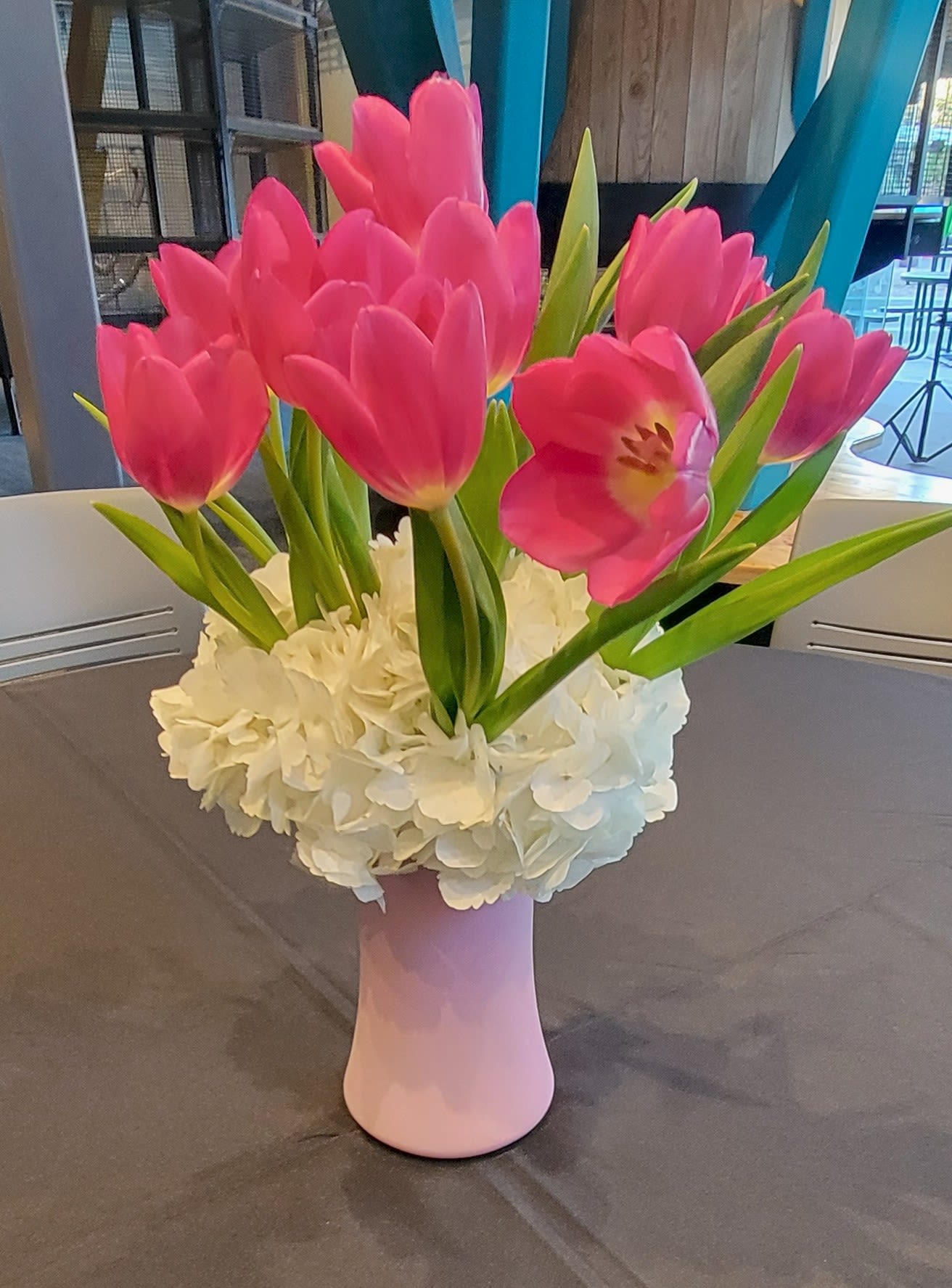 Pink tulips arranged in a pink vase with white flowers at the base