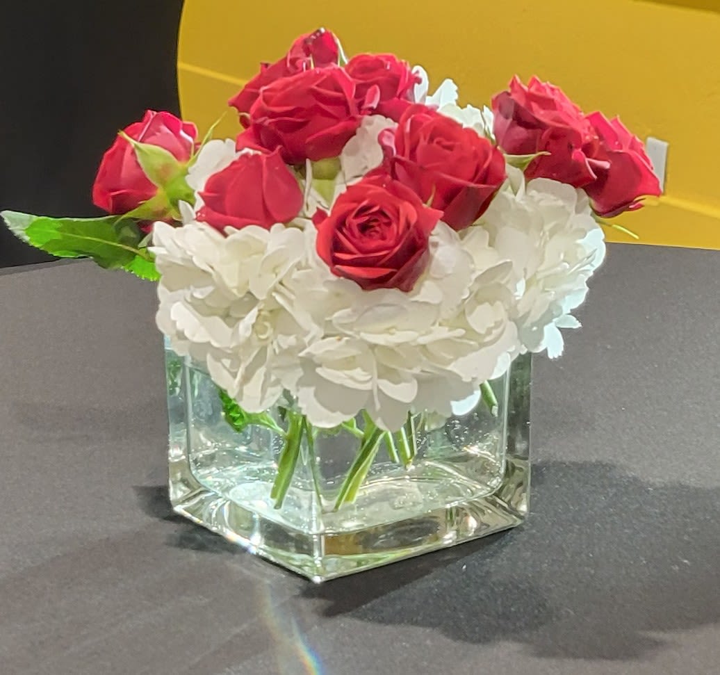 Red roses and white hydrangeas arranged in a clear square vase.