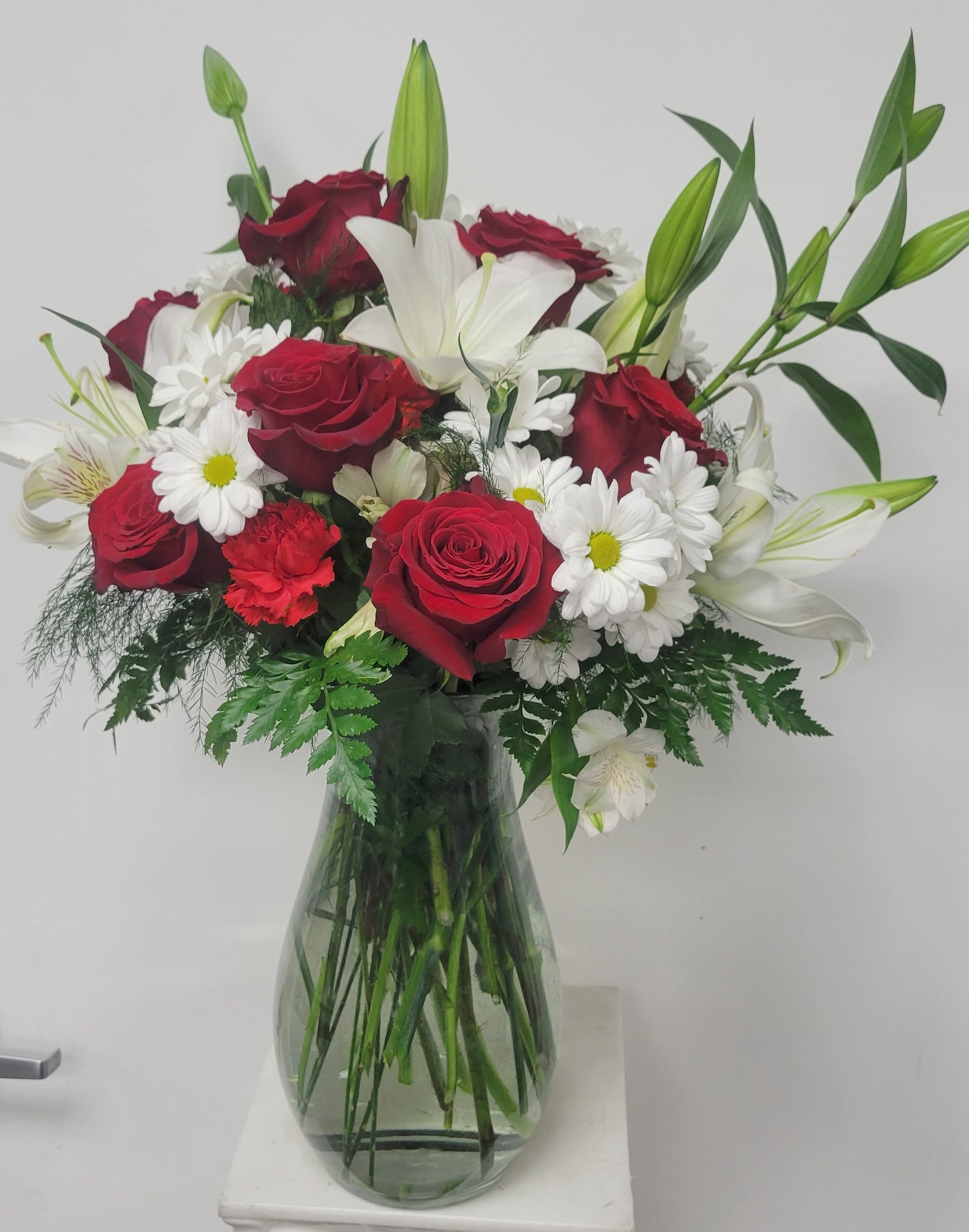 Bouquet of red roses, white lilies, and daisies in a glass vase