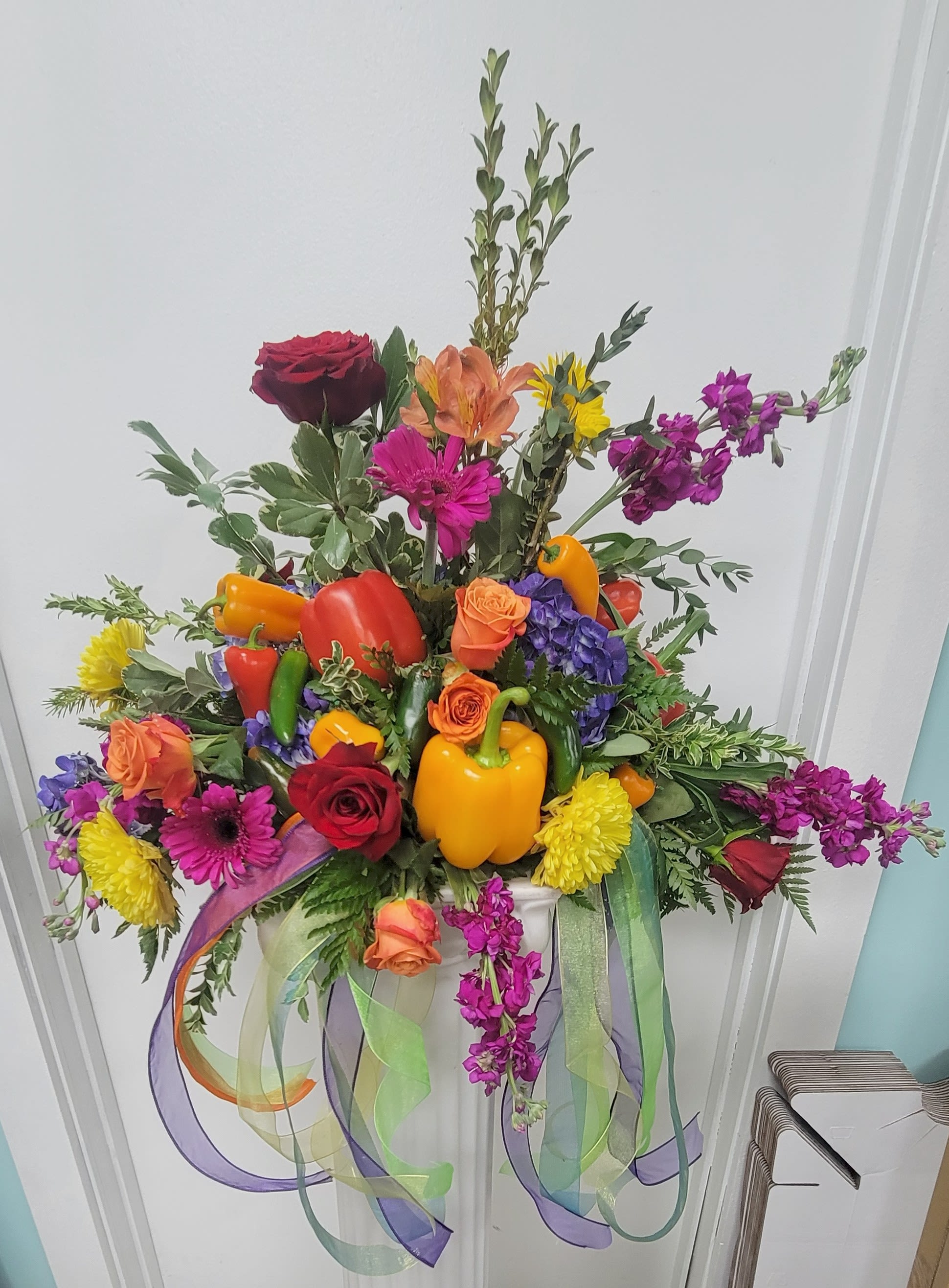Colorful floral arrangement with peppers and ribbon streamers in a white container