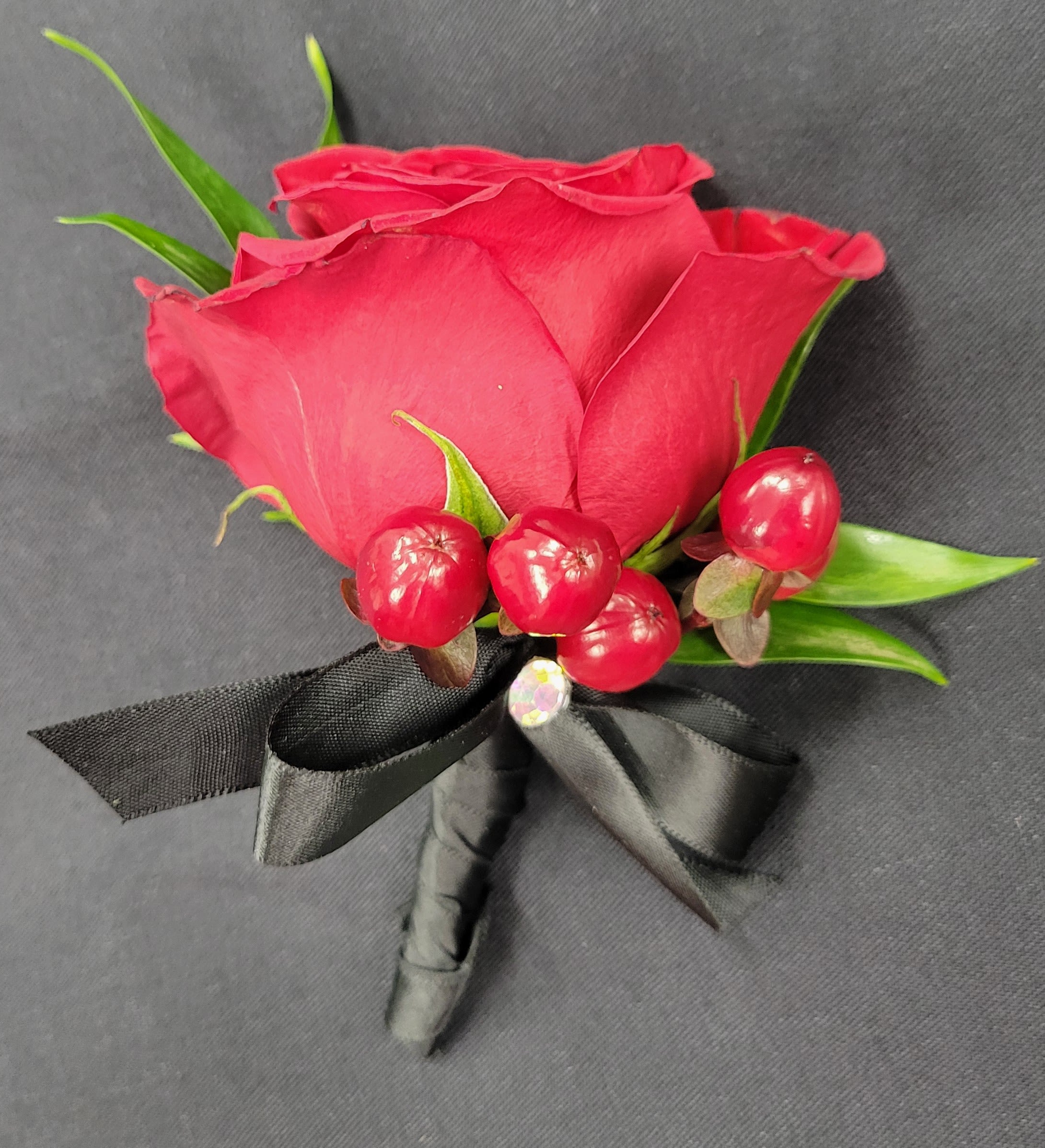Red rose boutonniere with berries and black ribbon