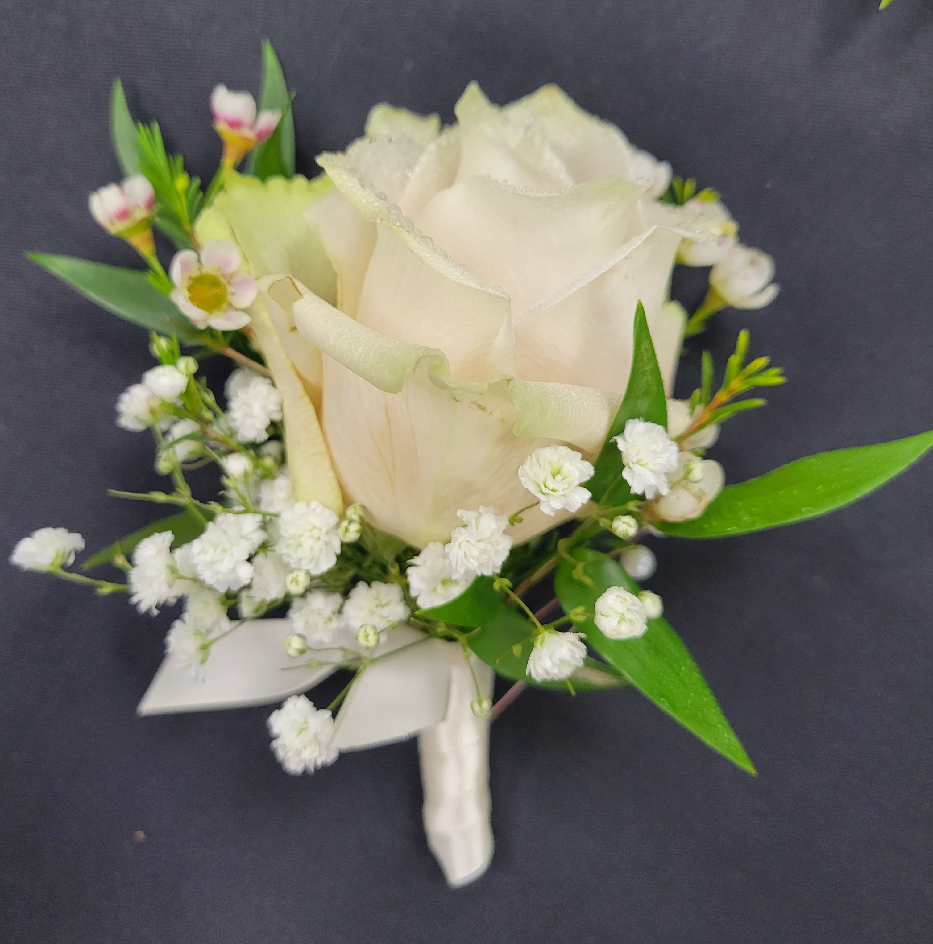 White rose boutonniere with baby's breath and green leaves